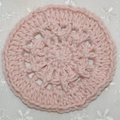 Crochet coaster in pale pink cotton with openwork pattern on white fabric