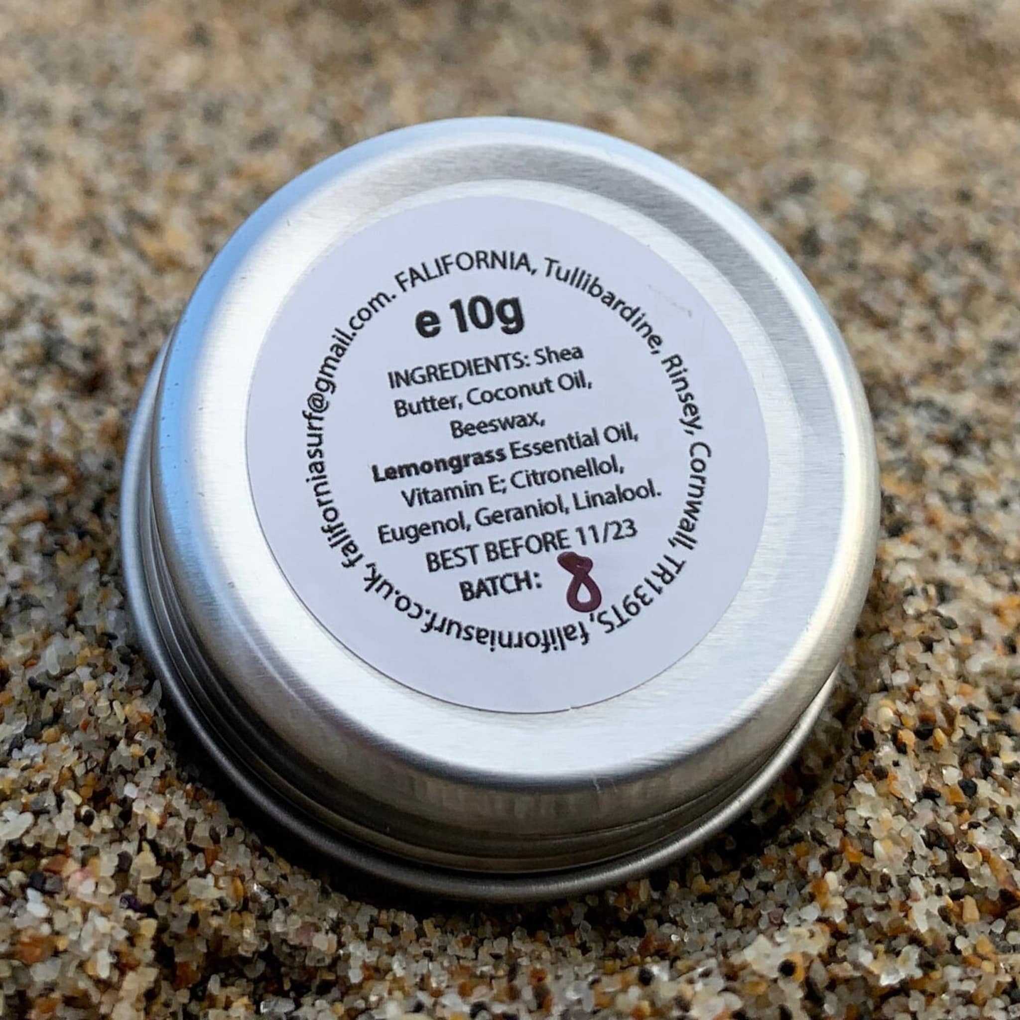 Metal tin with white label, silver lid, and text on sand background