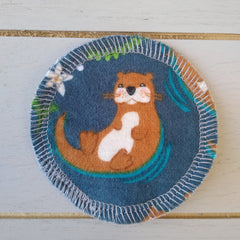 Coaster with otter print, blue fabric, white stitched edge, and floral accents
