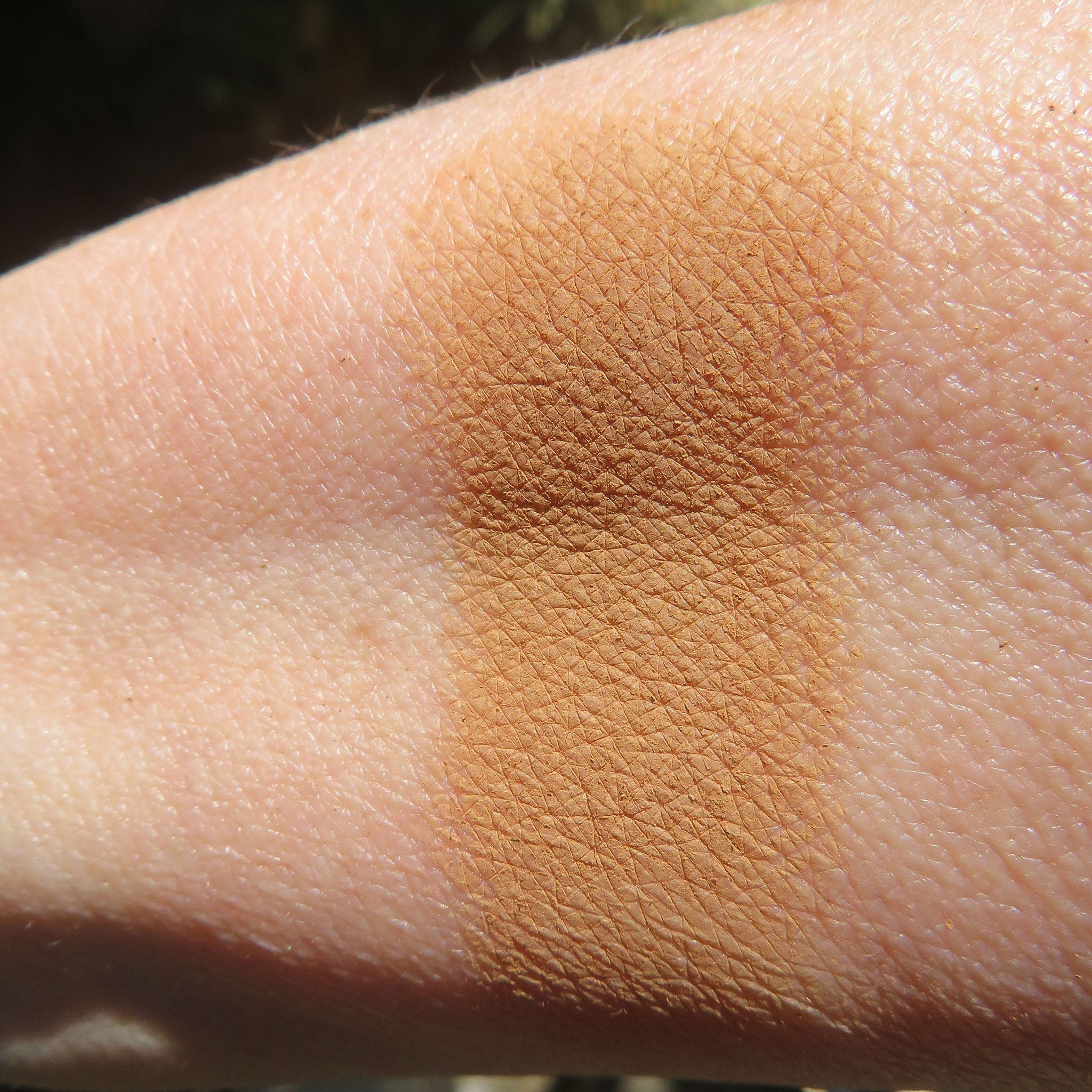 Side view of matte brown-orange mineral eye shadow powder spilling from jar onto marble surface