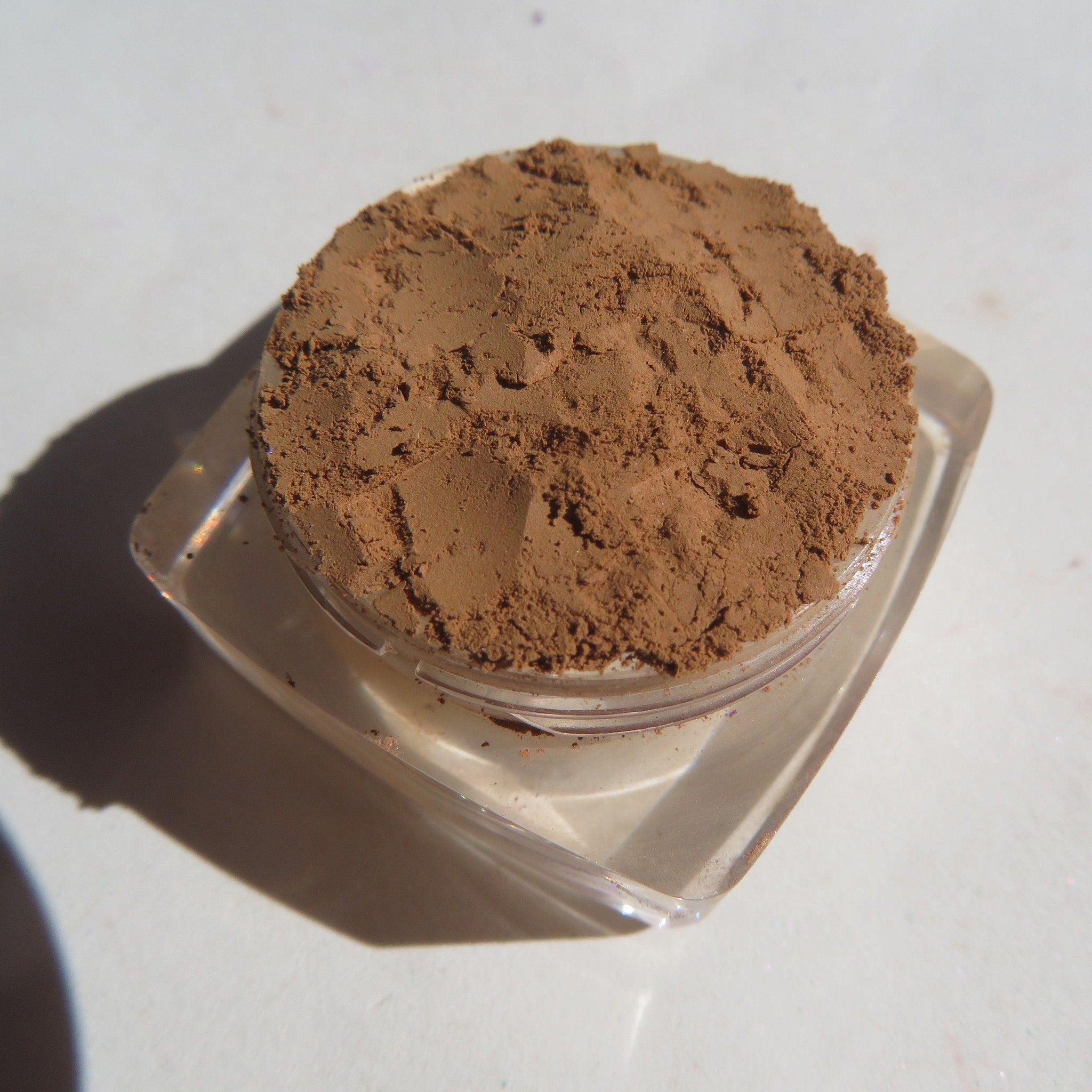 Close-up of matte brown-orange mineral eye shadow powder with loose pigment texture in a small jar