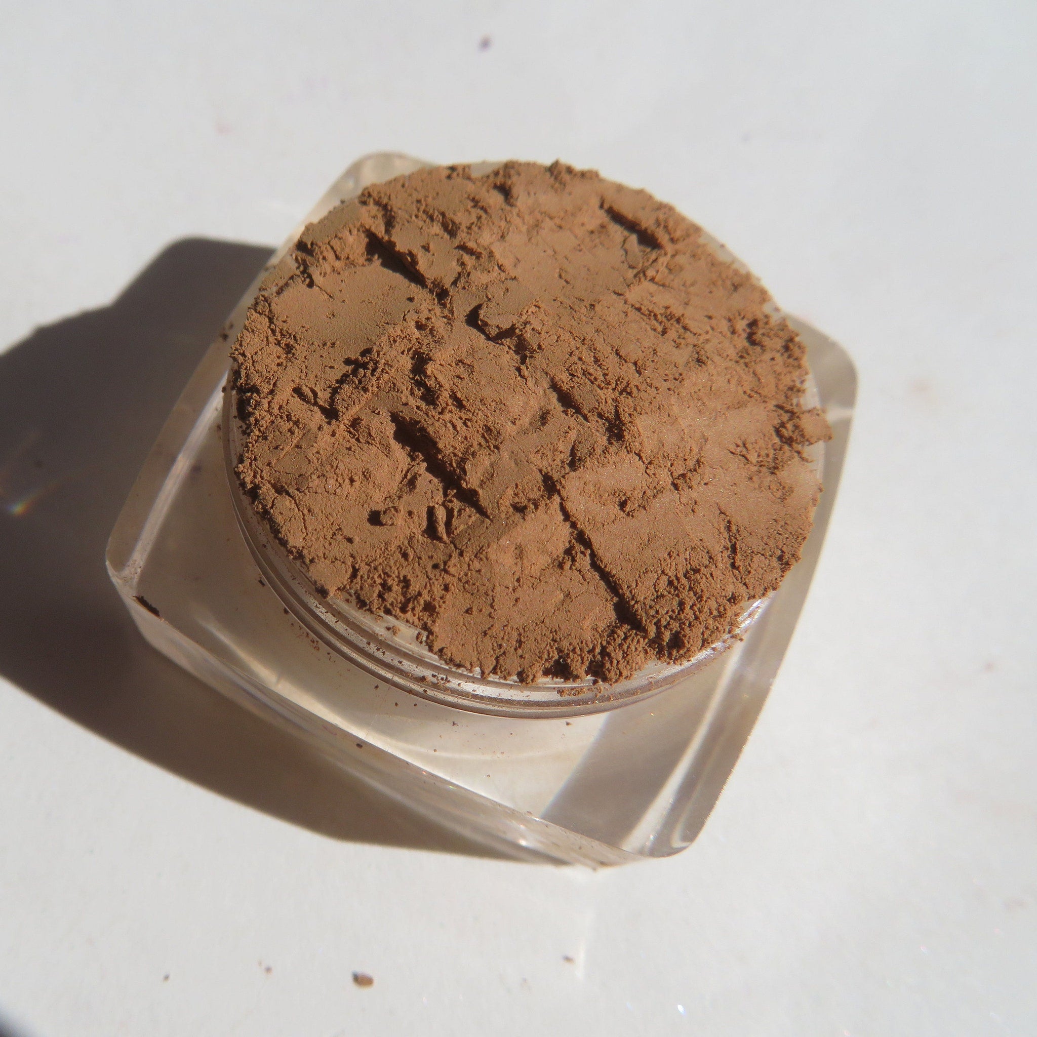 Close-up of matte brown-orange mineral eye shadow powder with fine loose pigment texture in a small jar