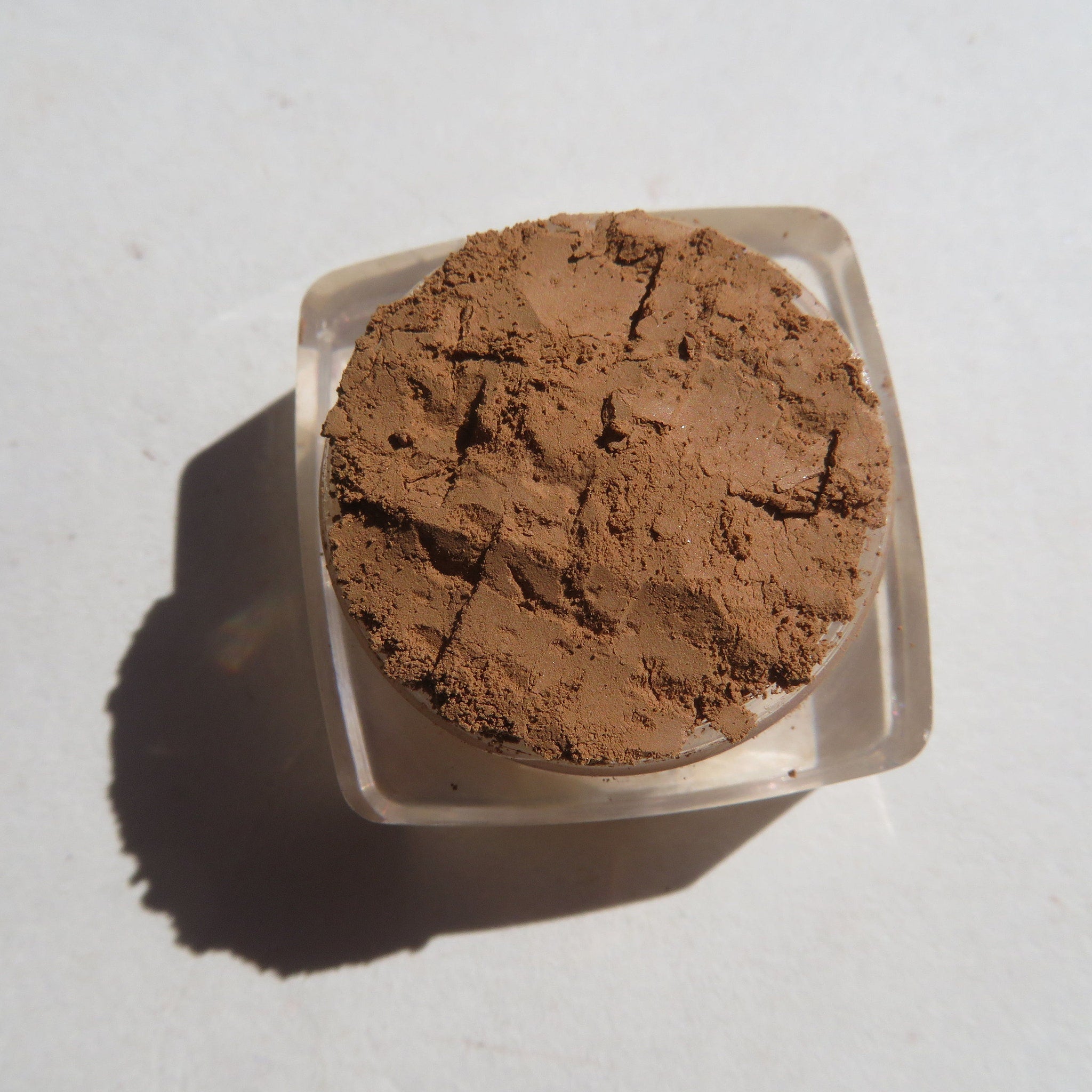Hand applying matte brown-orange mineral eye shadow with fingertip for a soft blended look