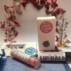 Lip balm tubes with peach and wildflower text, next to a gift box with a thank you sticker