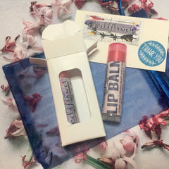 Lip balm tube with pink cap and label, in white box with wildflower text, on blue mesh fabric