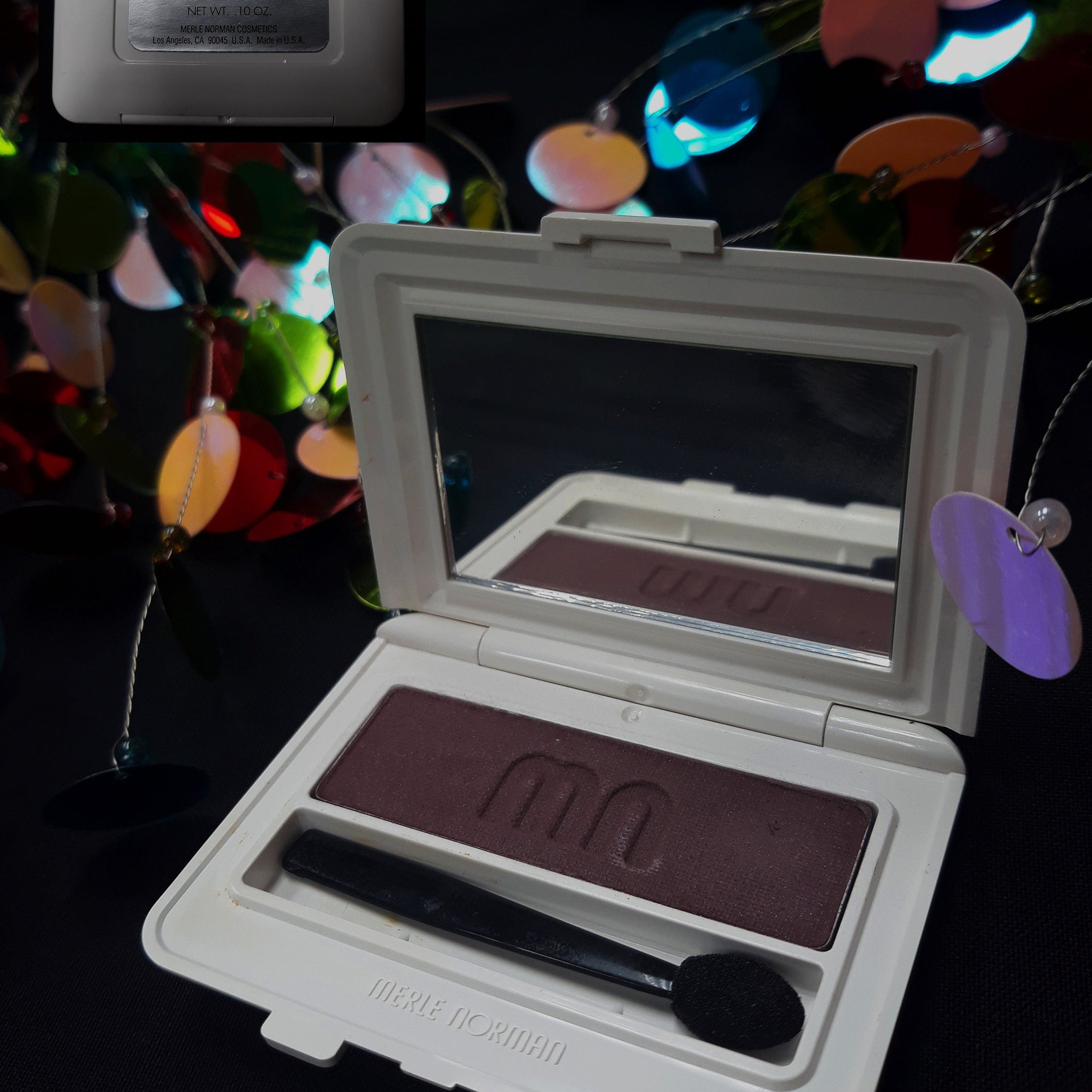 Close-up of Merle Norman Luxiva single eye shadow compact in shimmering plum with embossed logo