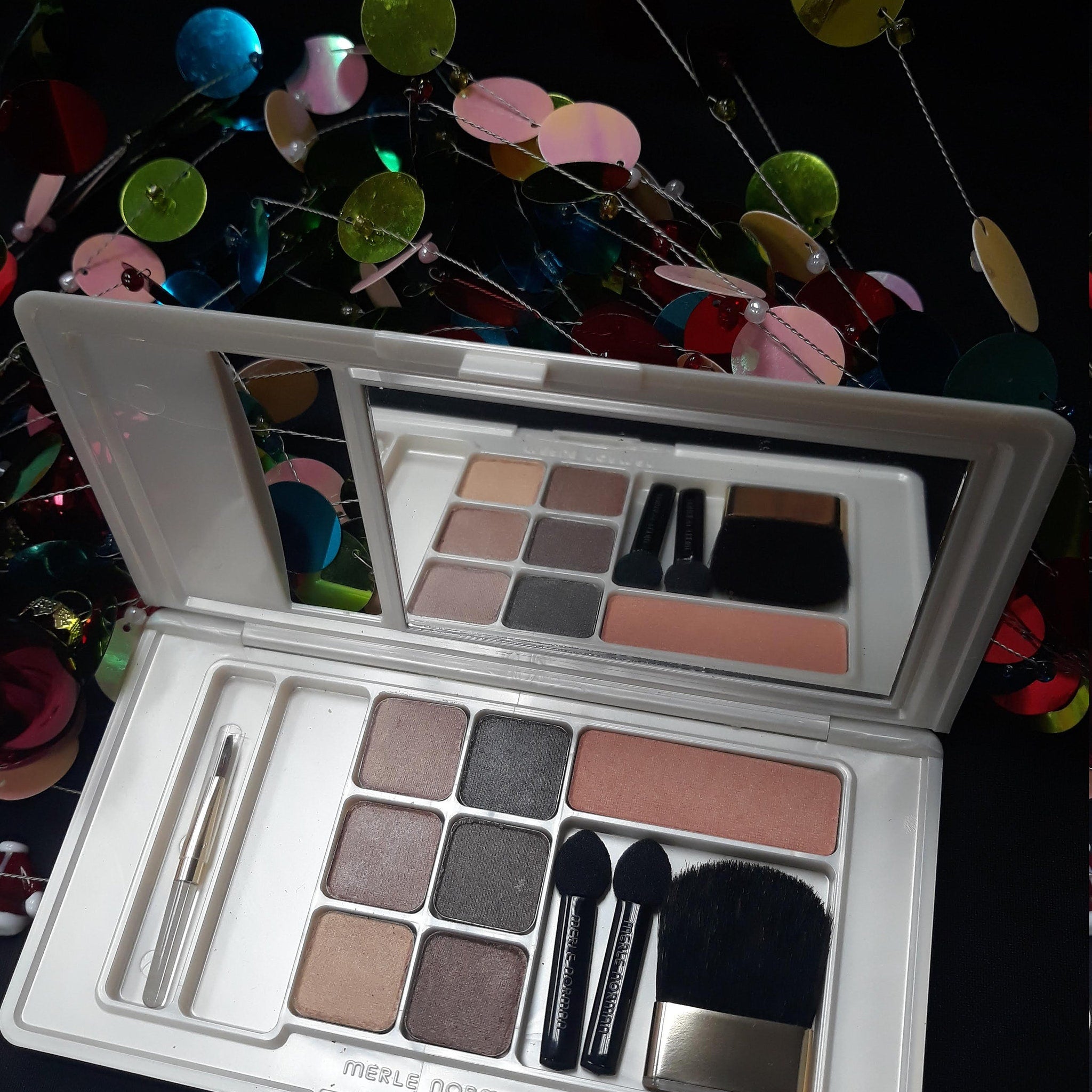 Close-up of Merle Norman Luxiva compact showing shimmering bronze and champagne eyeshadow shades with embossed logo