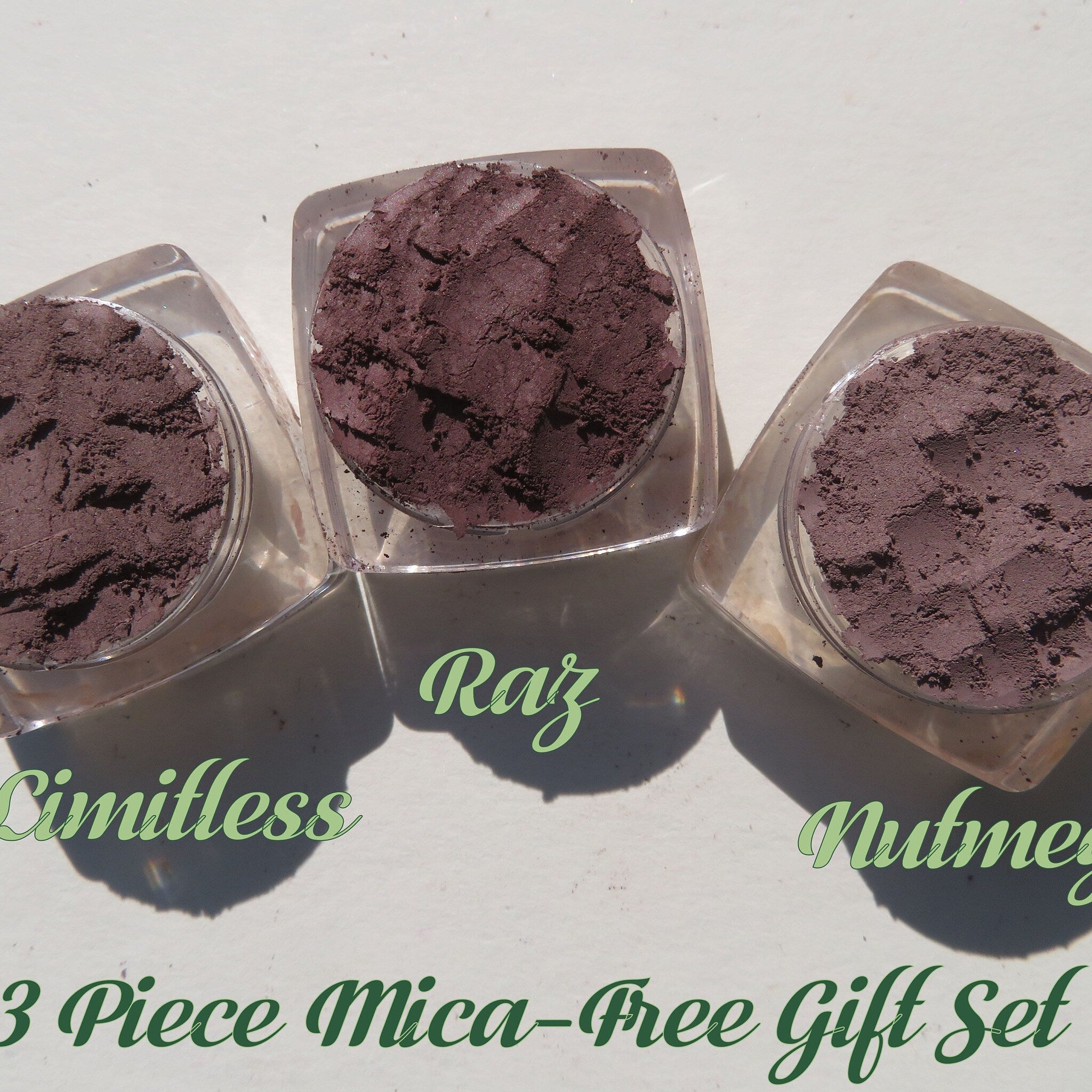 Overhead view of ten loose mineral eyeshadows in assorted matte and shimmer shades with small scoop for application