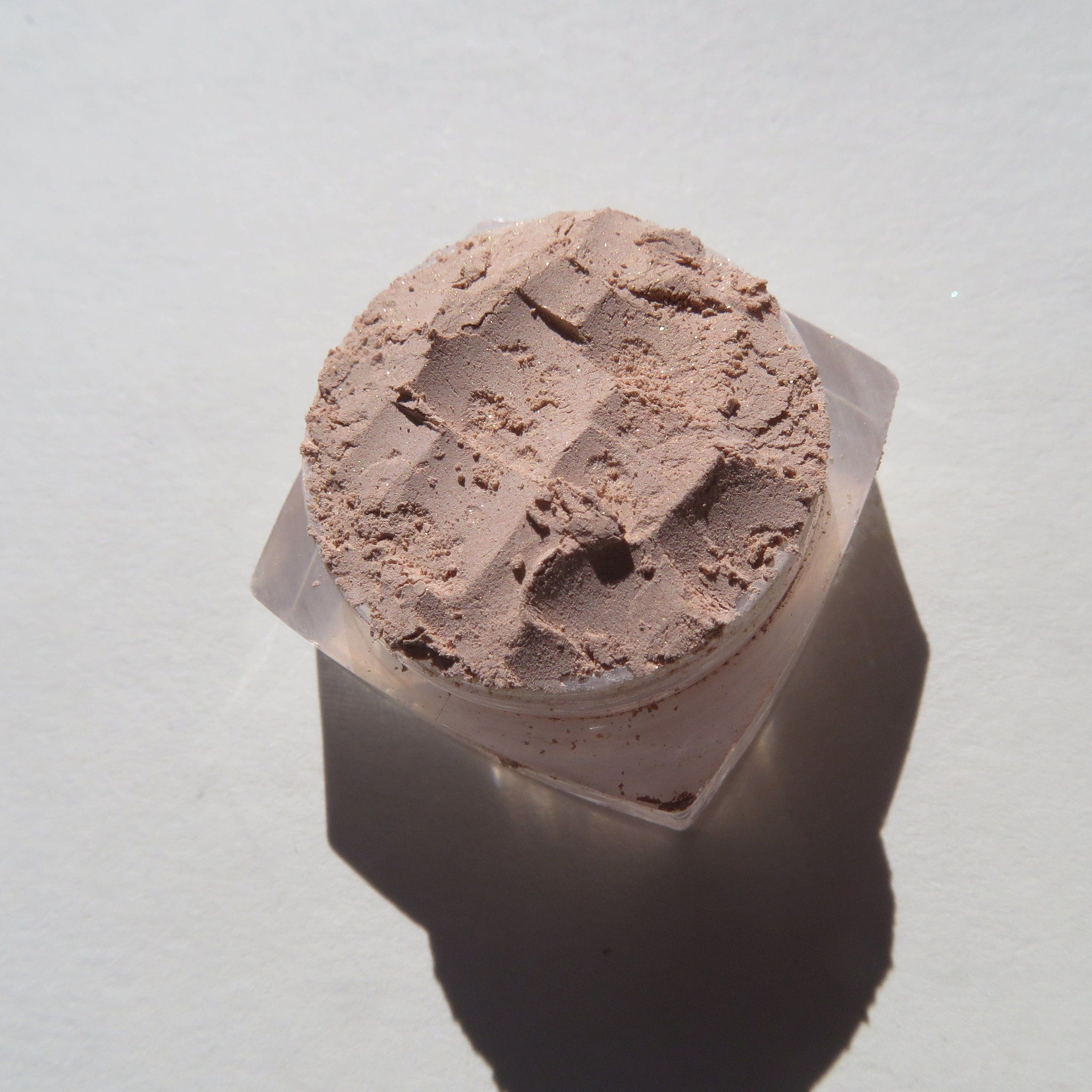 Close-up of loose shimmering SANDCASTLES eyeshadow in pale beige with sandy brown flecks, showcasing texture