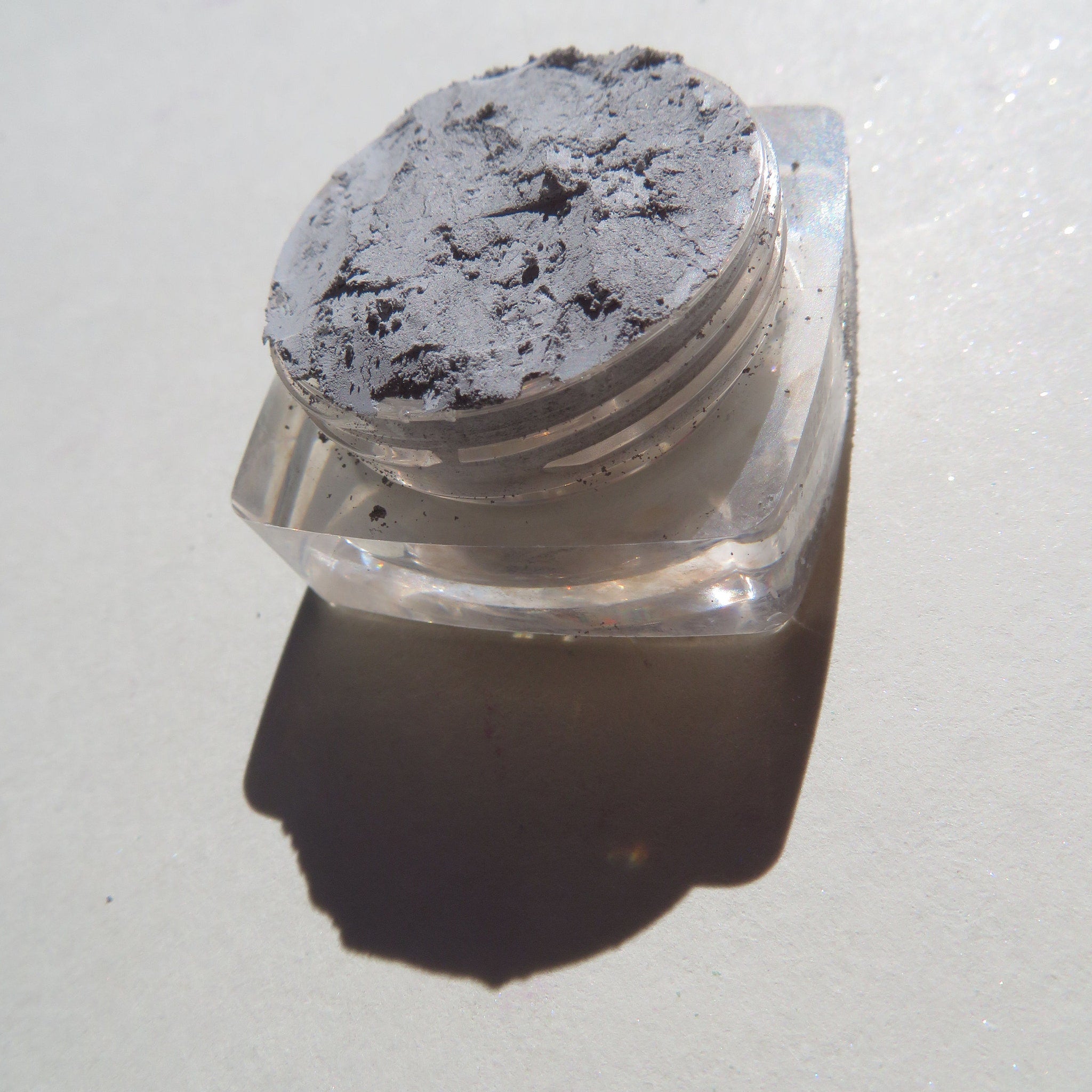 Open jar of matte gray Titan loose pigment eyeshadow with vegan label on minimalist white packaging