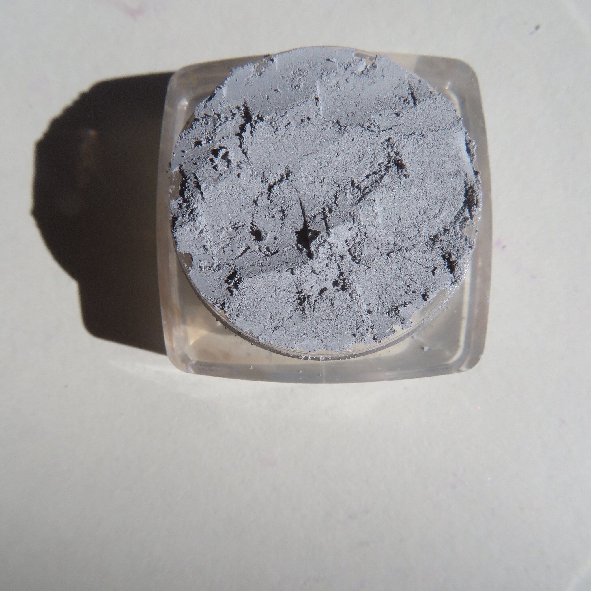 Close-up of matte gray loose pigment eyeshadow with fine powder texture in eco-friendly packaging