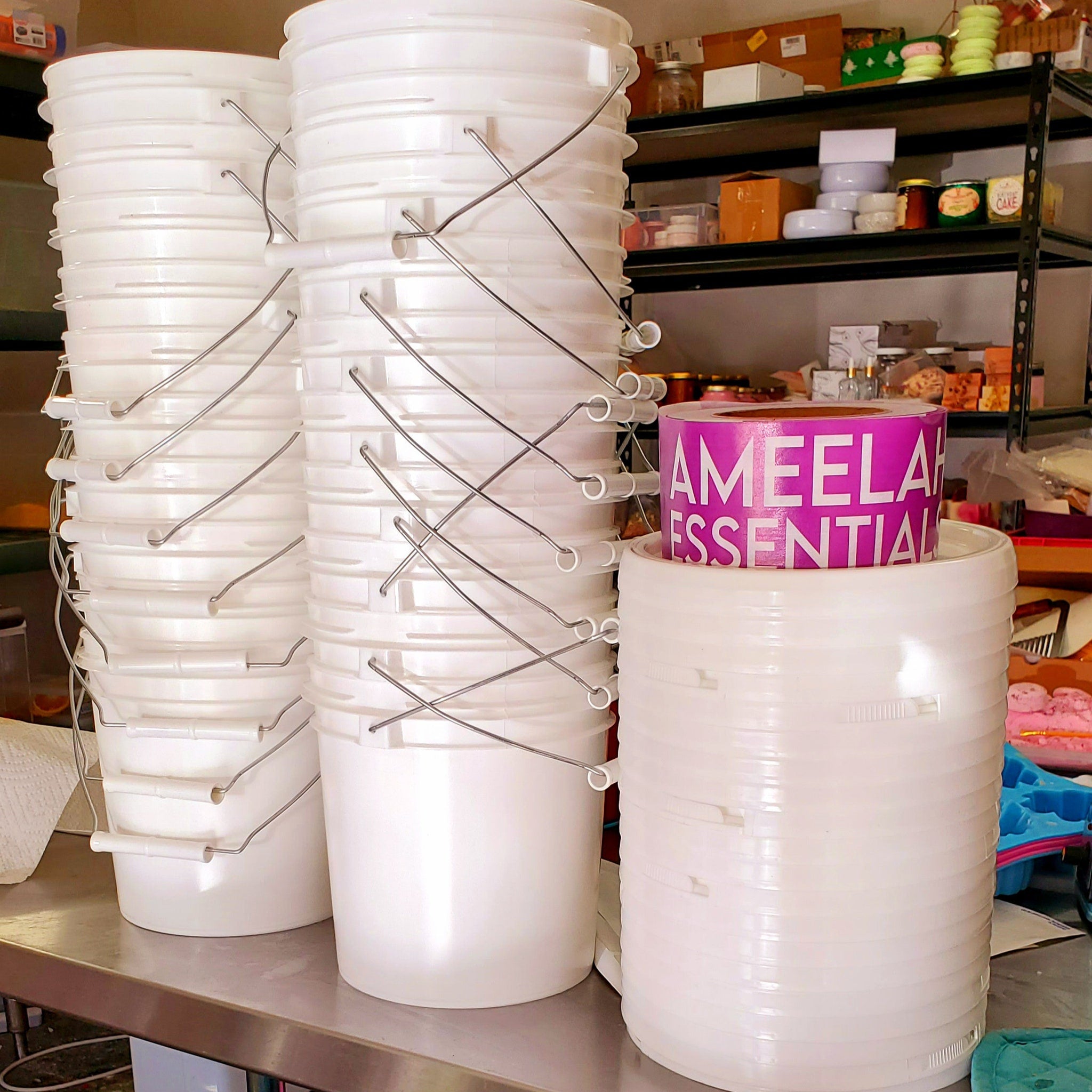 White plastic buckets with metal handles stacked, Ameelah Essentials label visible