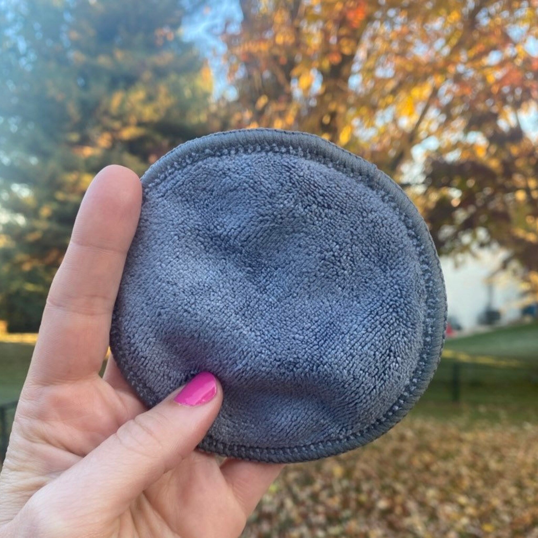 Reusable makeup remover pad, gray microfiber material, round shape held in hand