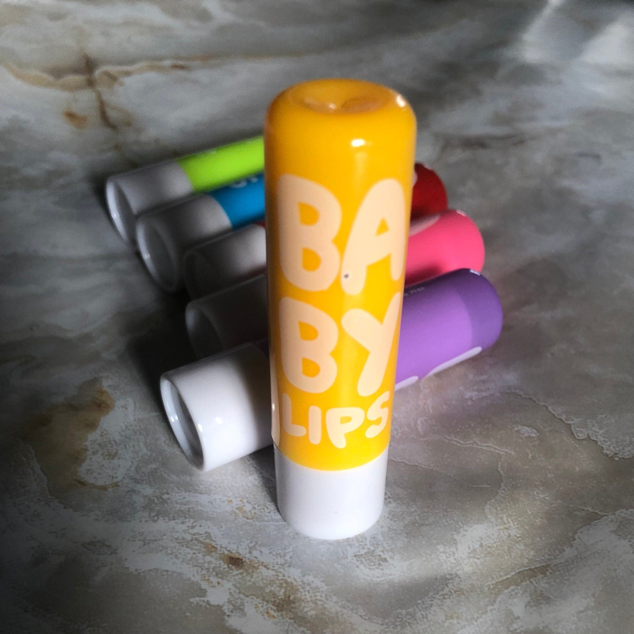 Lip balm tubes in yellow, white, pink, and purple with Baby Lips branding visible