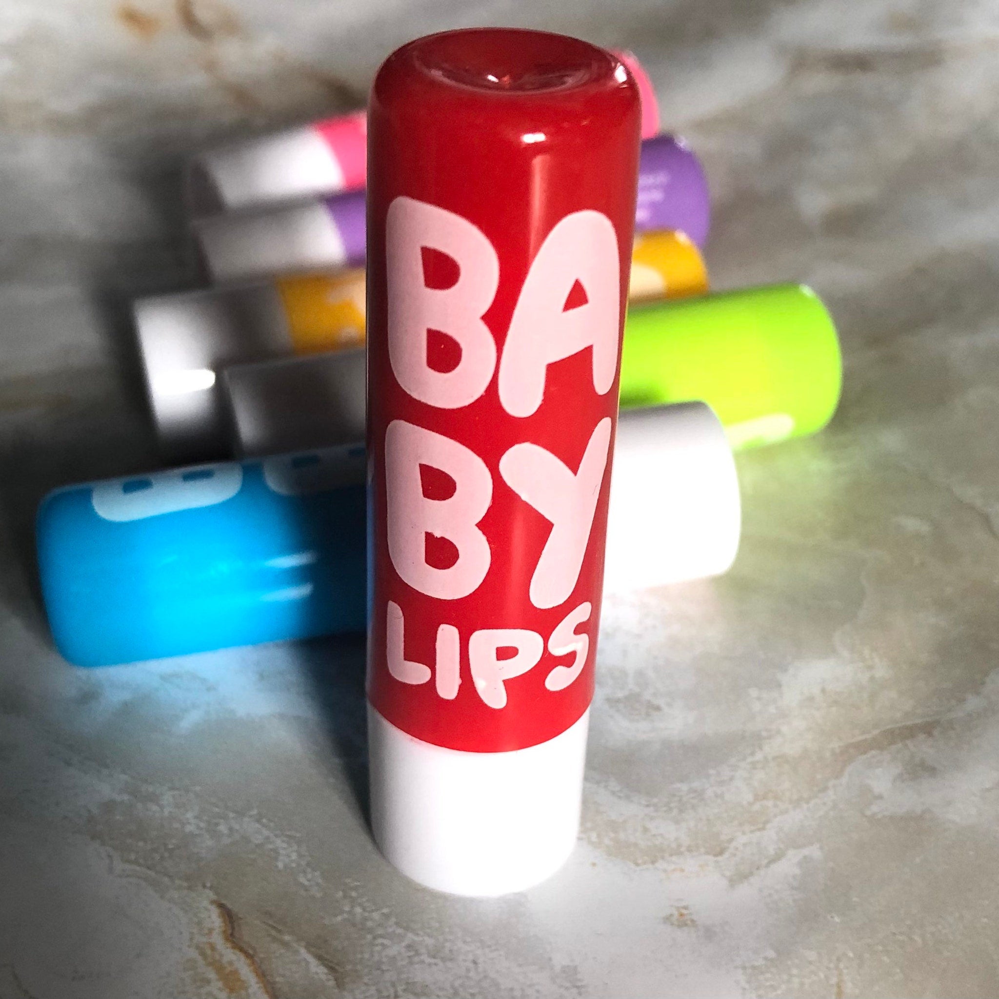 Lip balm with red and white tube, "Baby Lips" text, and other colorful tubes in background