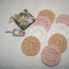 Crochet coasters in white, tan, and pink colors with floral pattern on a white surface