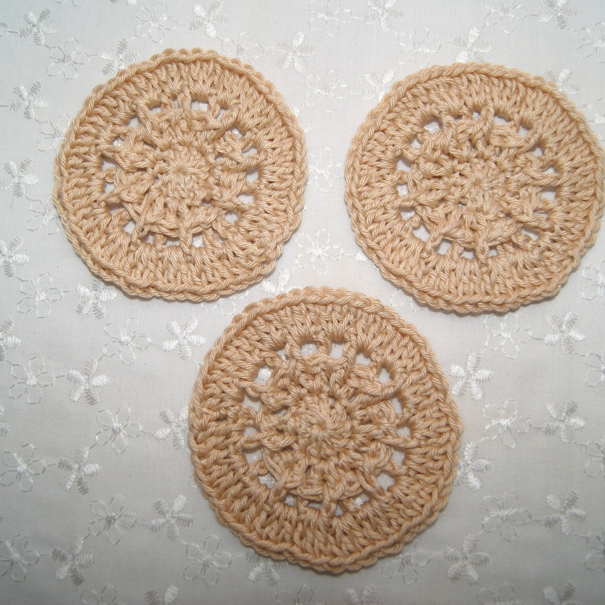 Crochet coasters in beige yarn, circular design, placed on floral fabric