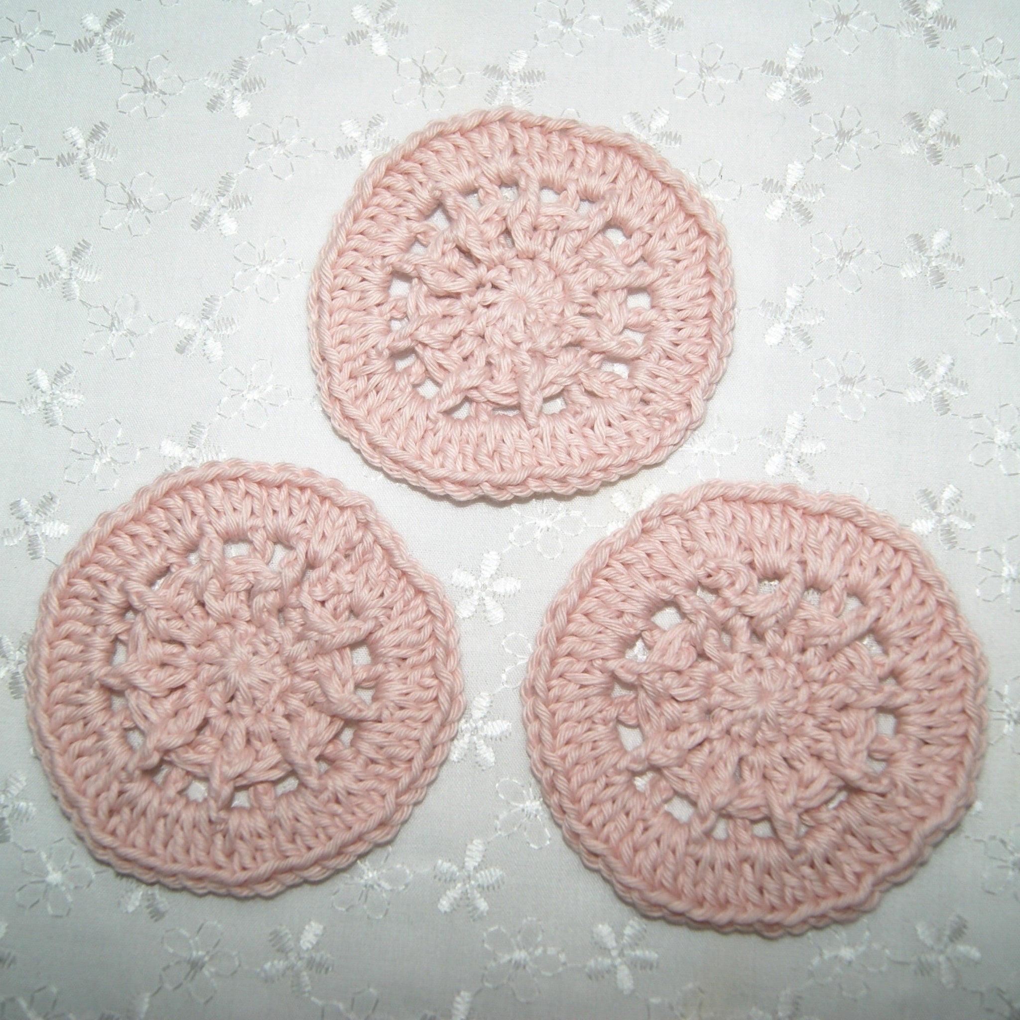 Crochet coasters, light pink cotton, circular design, placed on floral fabric
