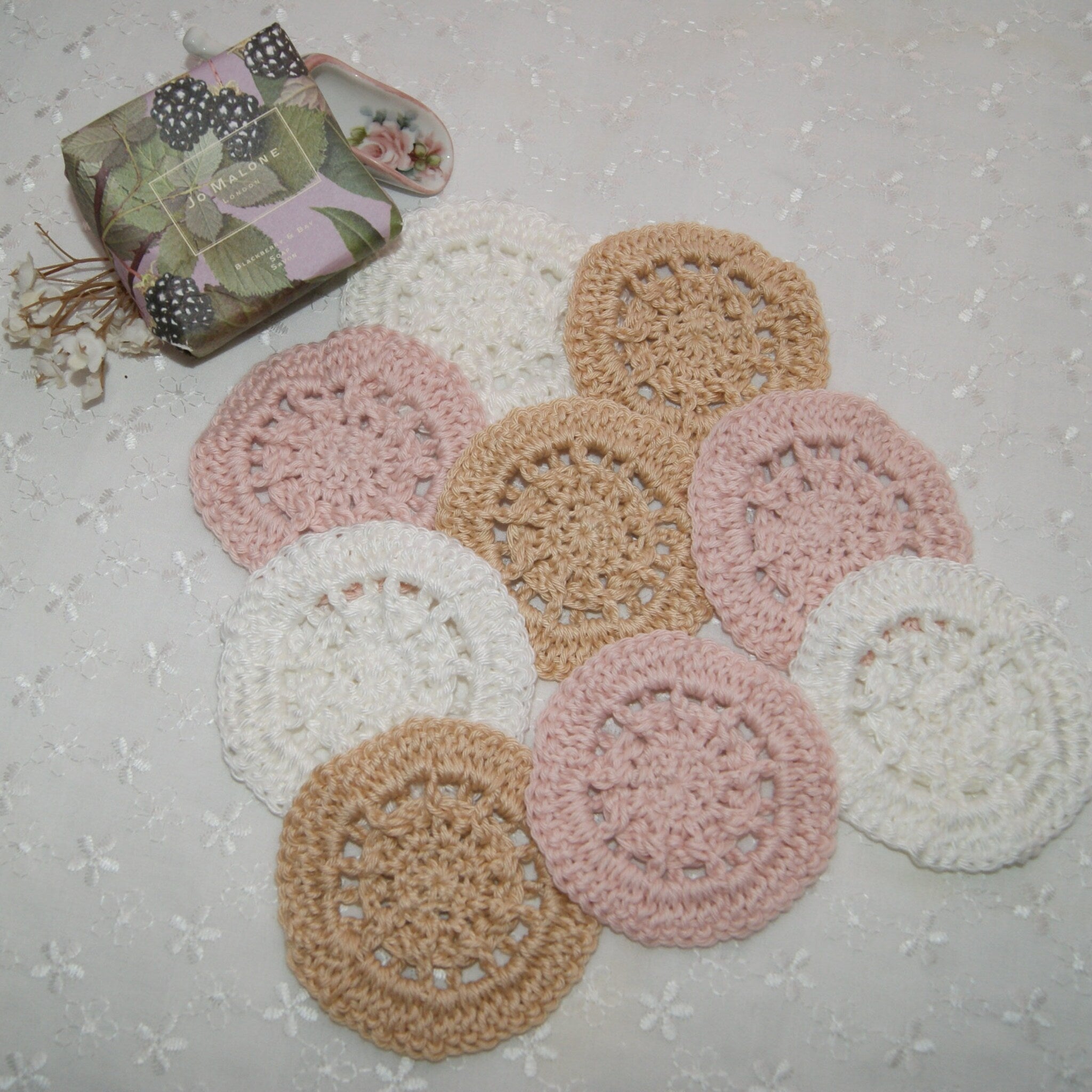 Crochet coasters in white, pink, and tan with circular pattern arranged on white fabric
