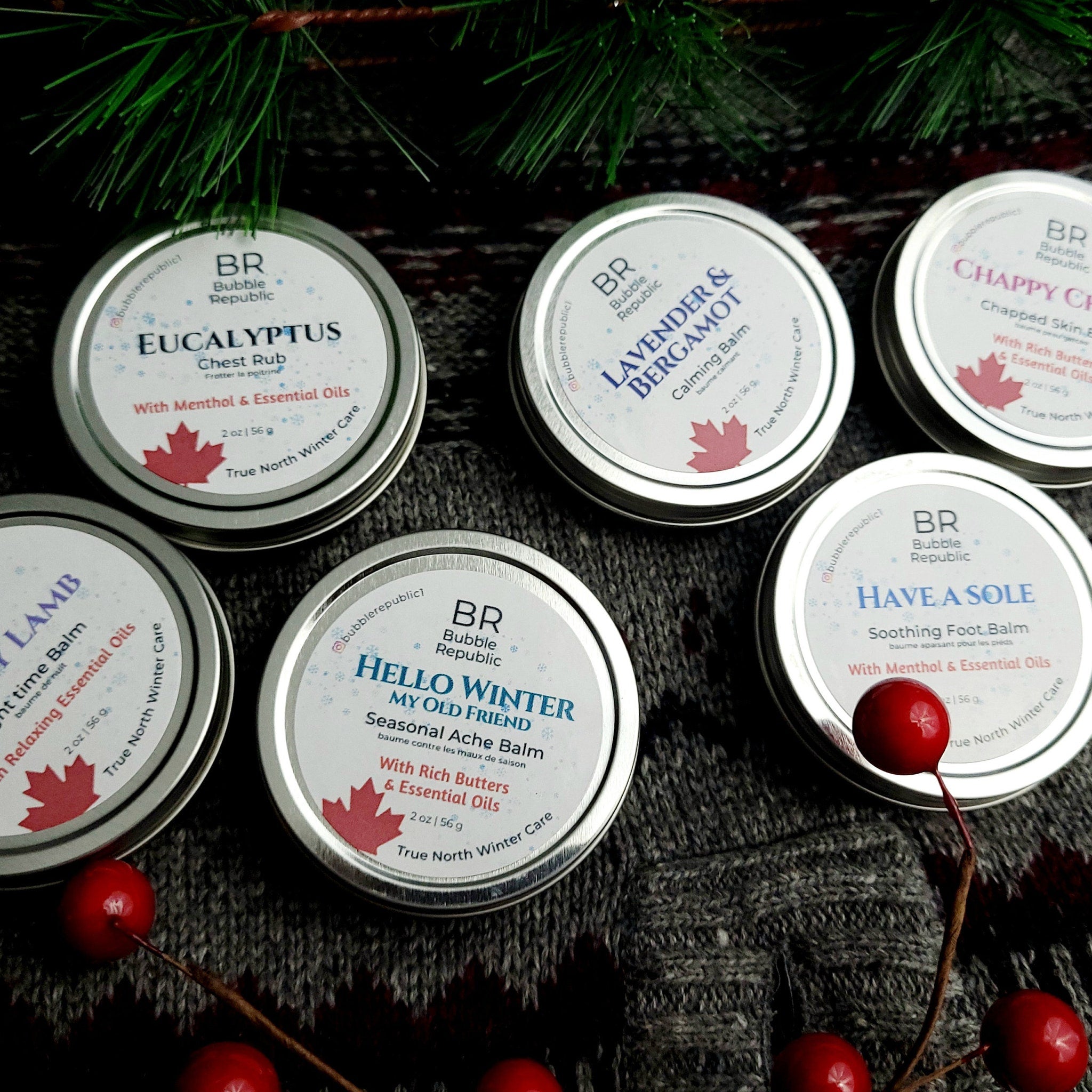 Body balms in silver tins with text, Bubble Republic brand on gray sweater background