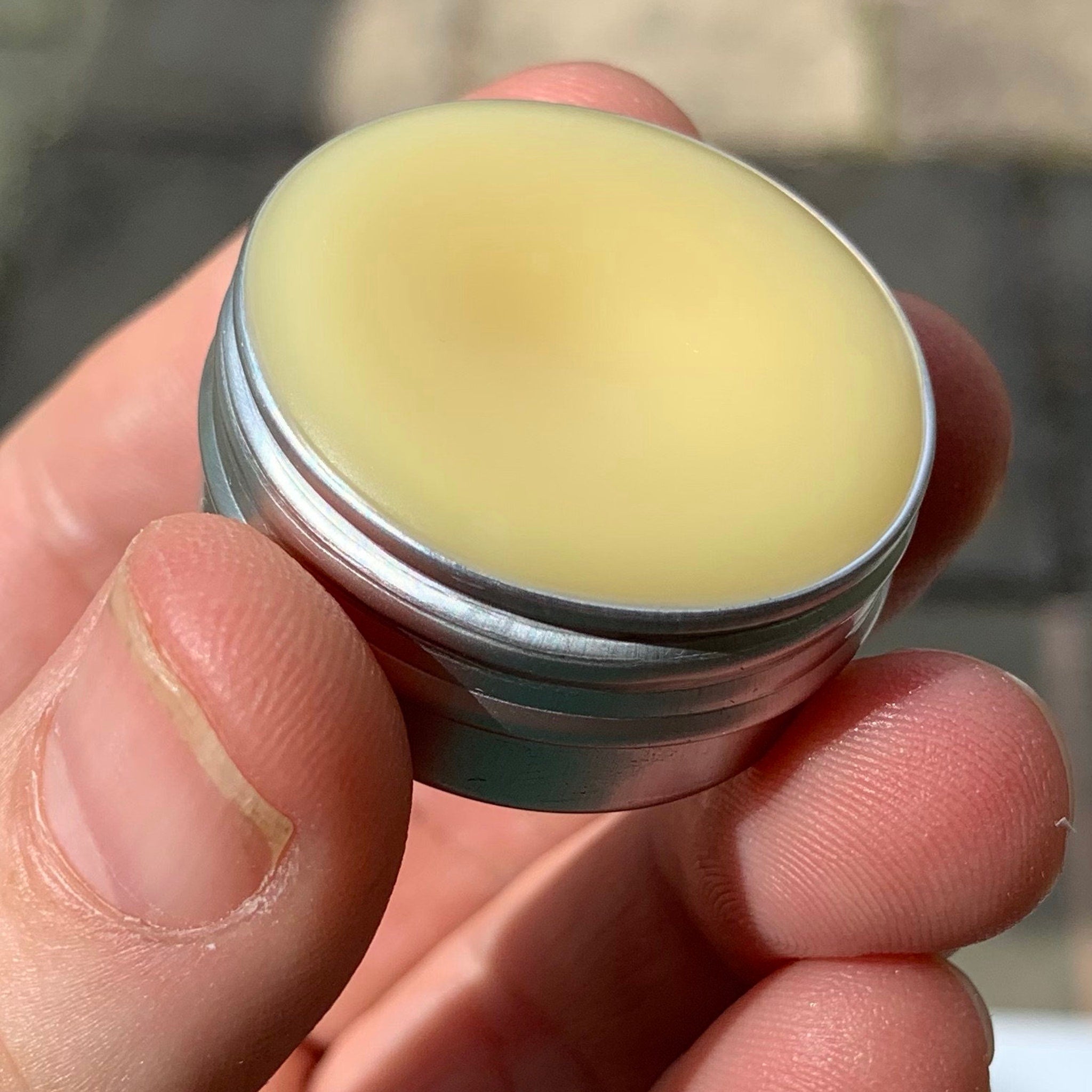 Lip balm in silver metal tin with yellow balm, held in hand