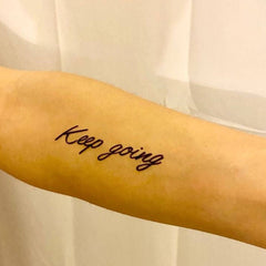 Temporary tattoo with black script on arm, "Keep going" text, skin tone background
