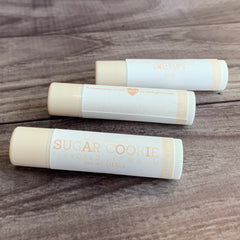 Lip balm tubes with white labels, beige tops, and text "SUGAR COOKIE" and "SWEET LIPS" on them.