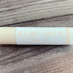 Sugar cookie lip balm tube, off-white and peach text on white label, on wood background