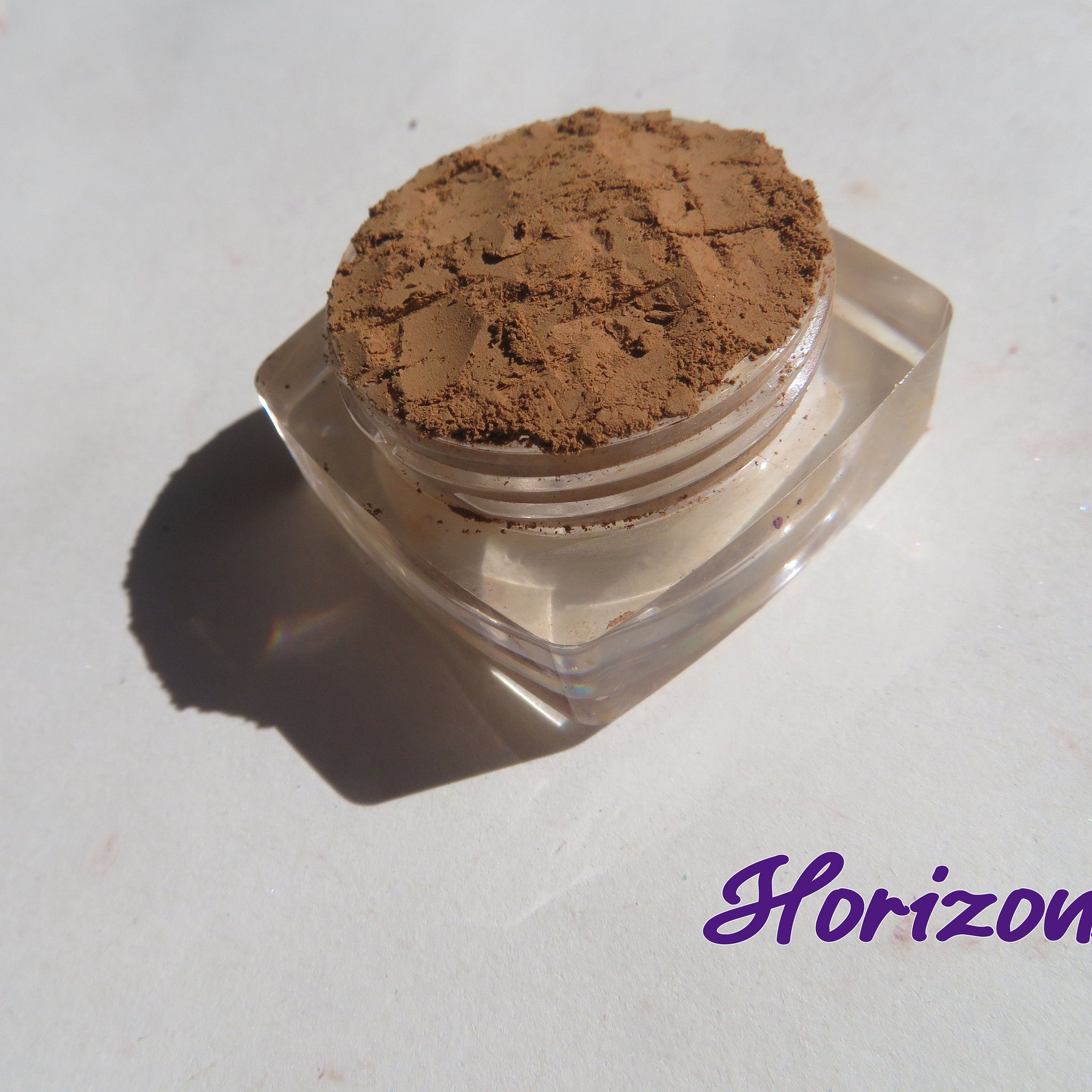 Open jar of matte brown orange mineral eye shadow with loose powder visible inside