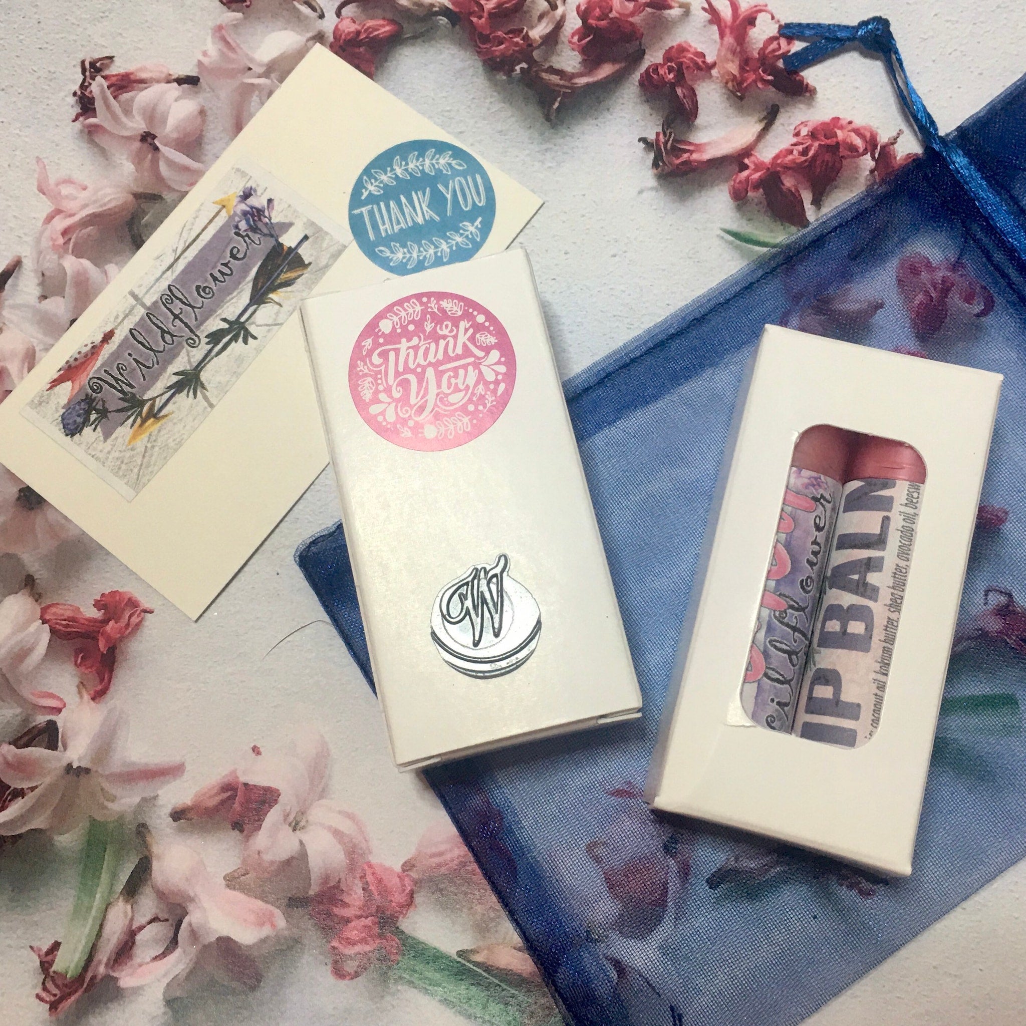 Lip balm in white box with wildflower pattern and "IP BALM" text, next to thank you cards