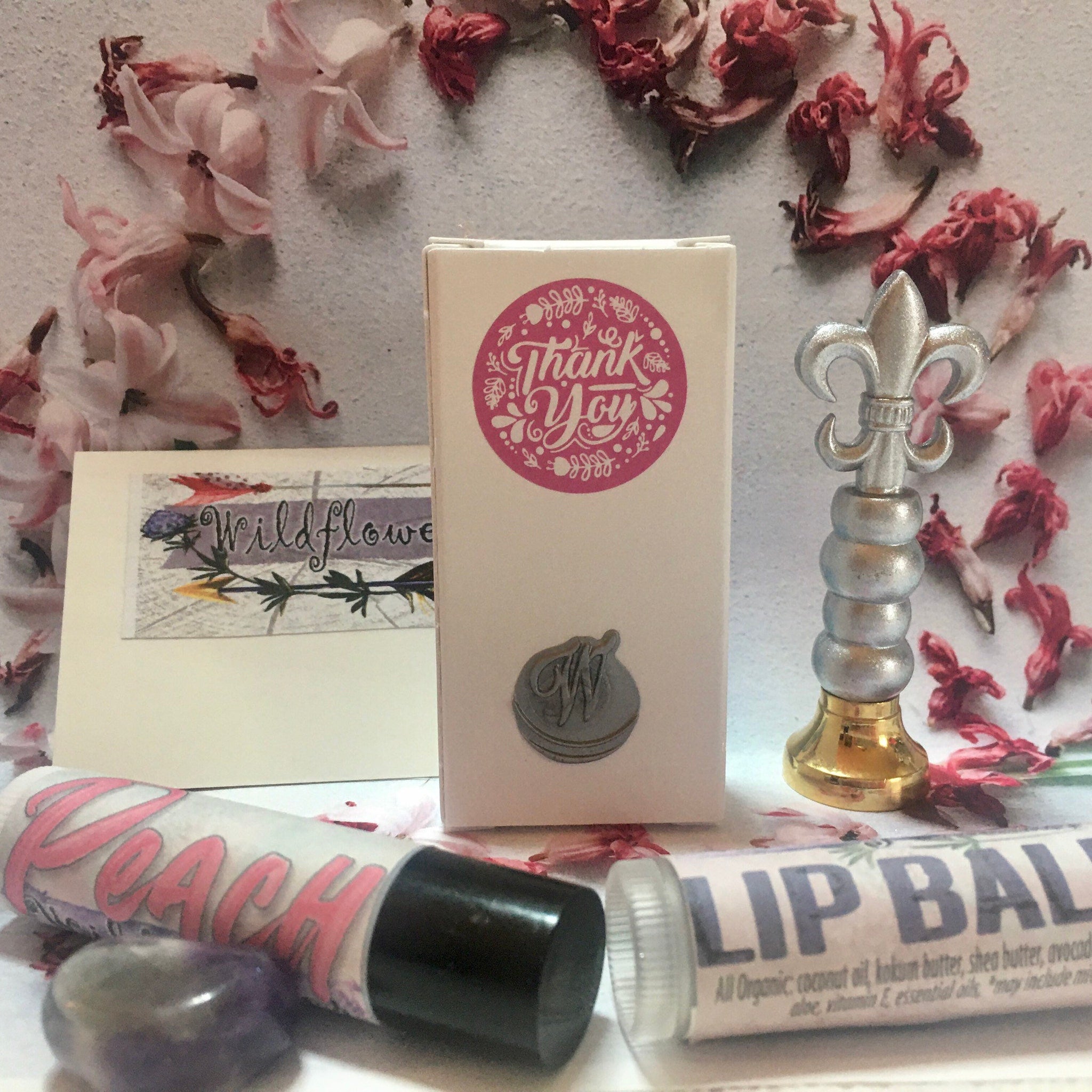 Lip balm tubes with peach text, white packaging and black caps, near a thank you sticker