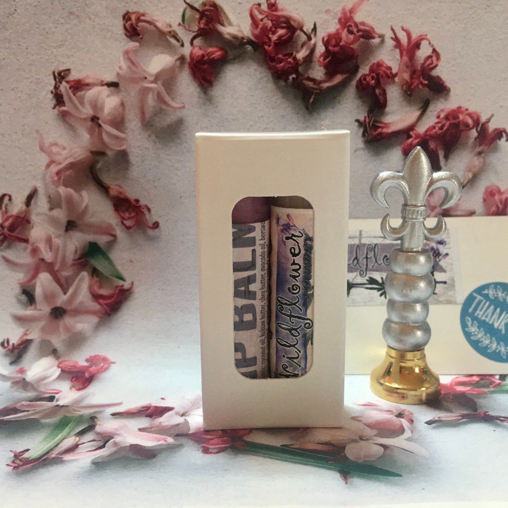 Lip balm in a cream box with "BALM" and "Wildflower" text, floral background.