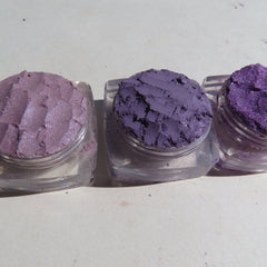 Close-up of fingers applying shimmering purple loose pigment eyeshadow with a brush