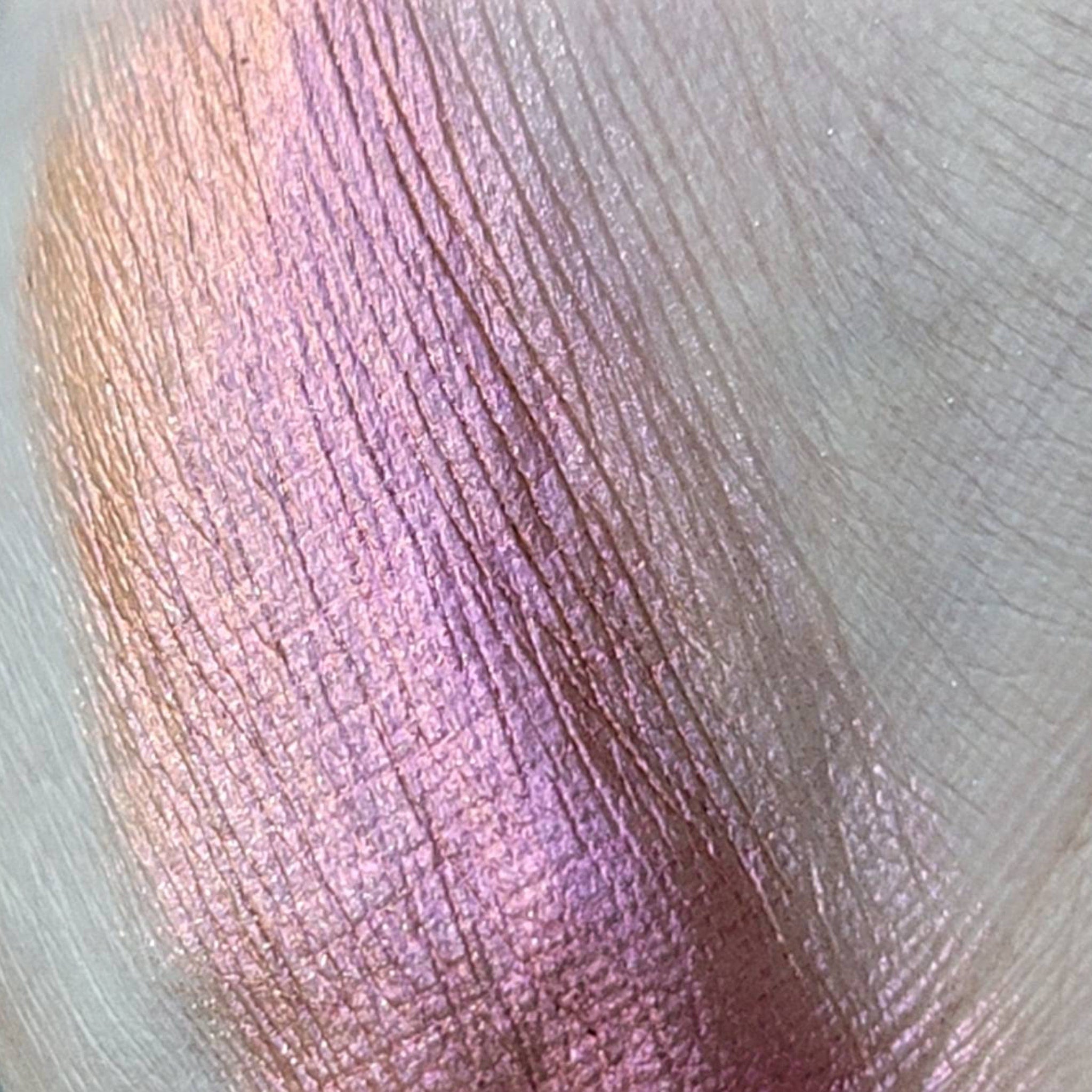 Side angle of pressed multichrome eyeshadow pan showing shimmering orange-to-pink shift in natural light