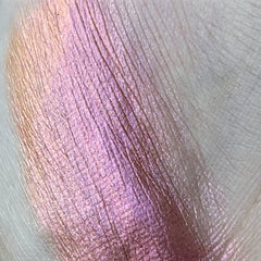 Side angle of pressed multichrome eyeshadow pan showing shimmering orange-to-pink shift in natural light
