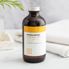 Organic face wash, brown glass bottle with silver cap, Conscious Skincare label visible