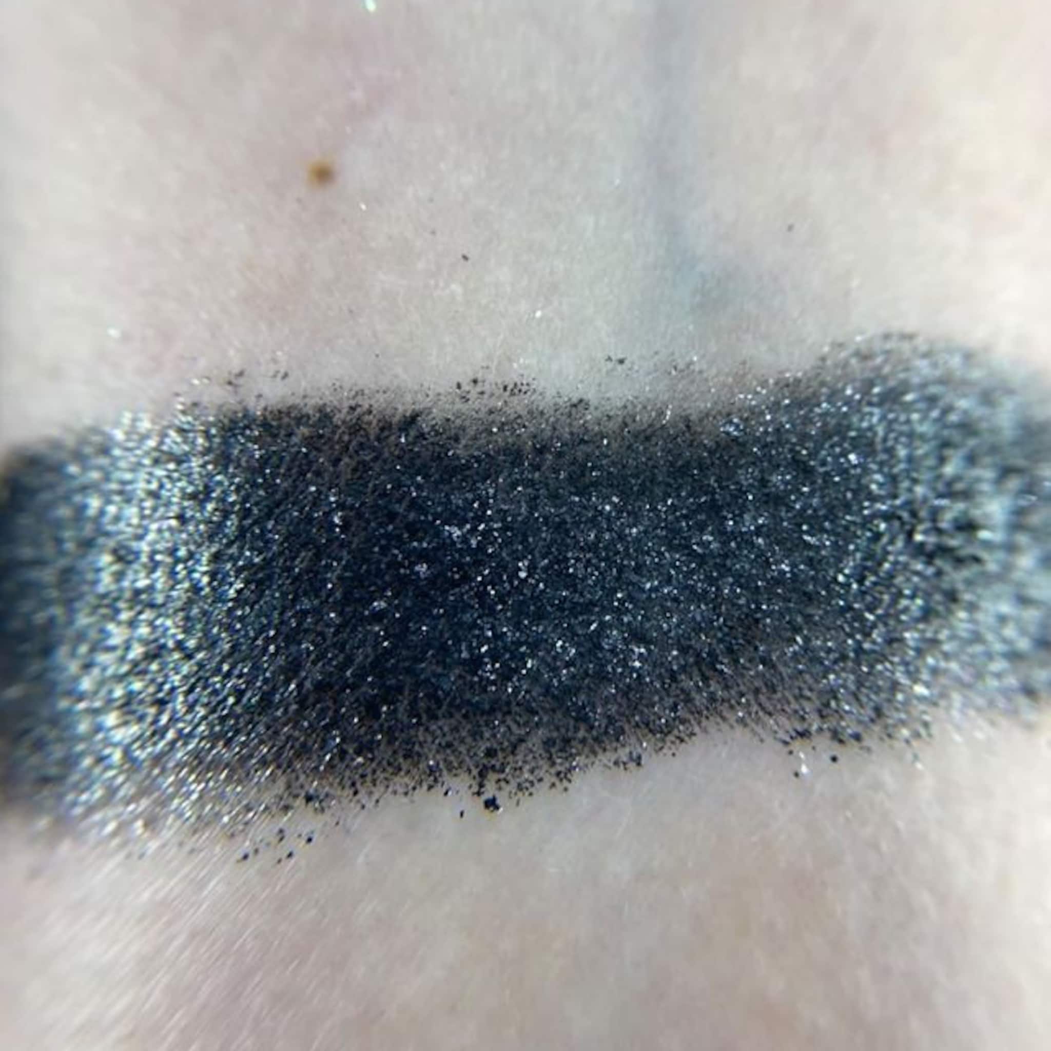 Close-up of six shimmering eyeshadow pans in bronze, gold, rose, plum, taupe, and navy with metallic finishes