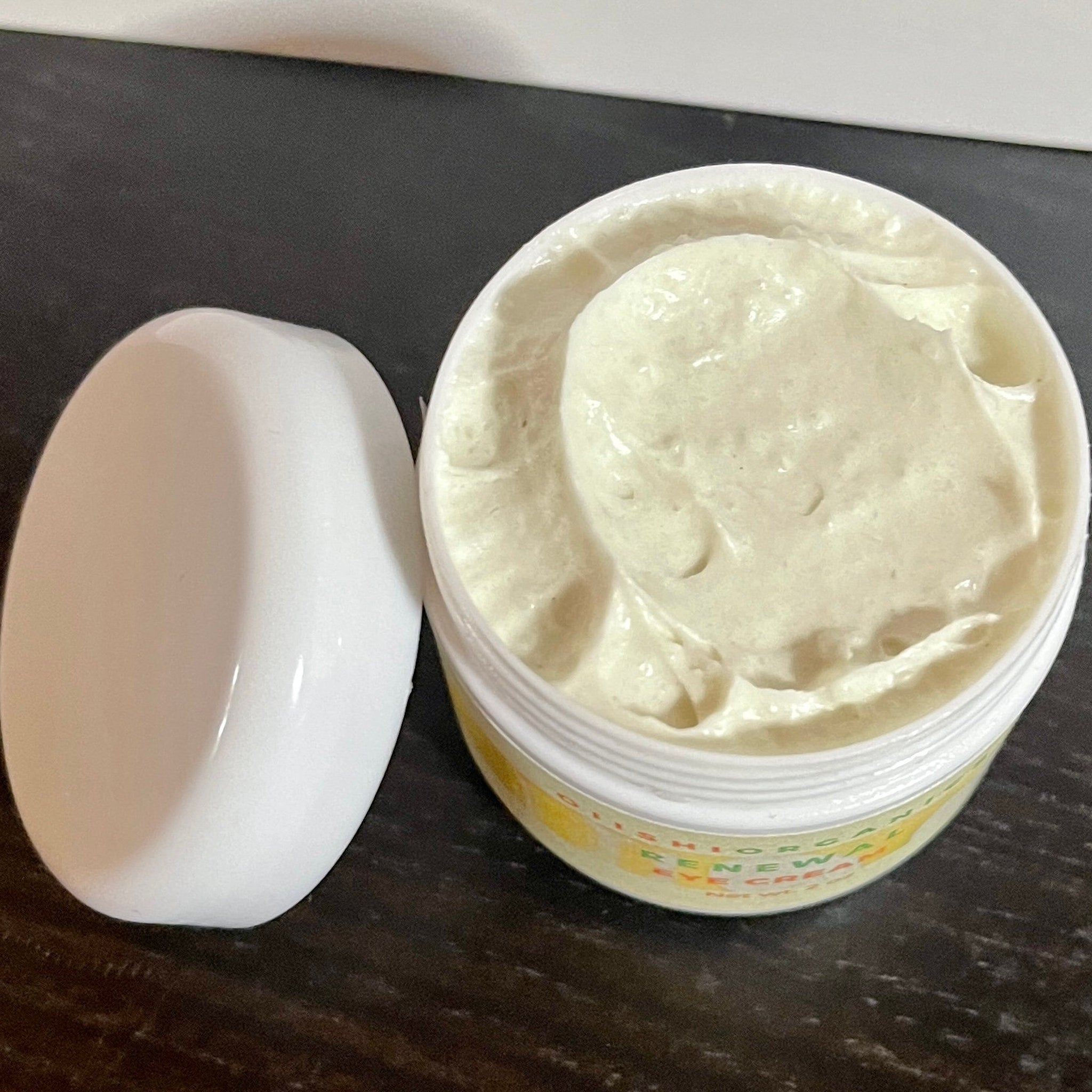 Eye cream jar, white plastic container with cream, yellow label visible, lid beside container