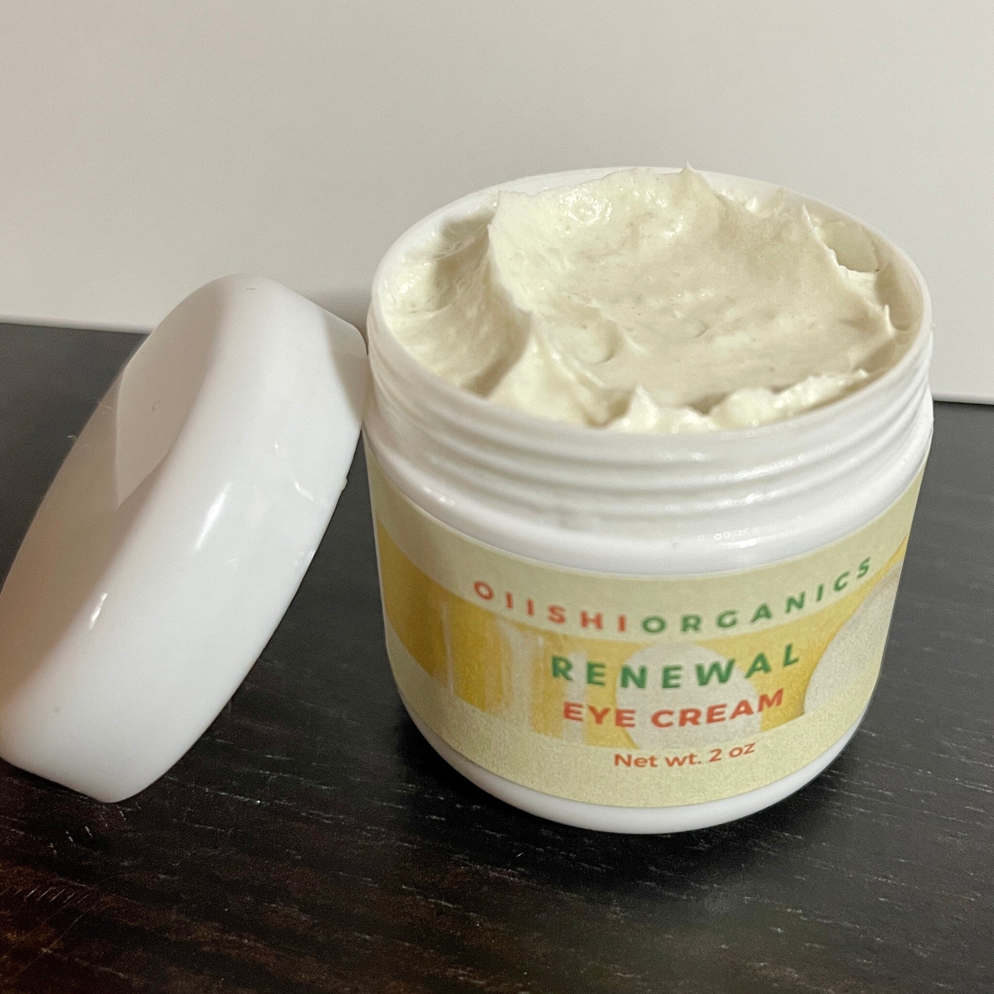 Eye cream in white jar with off-white cream and OIIISHI ORGANICS label on dark surface
