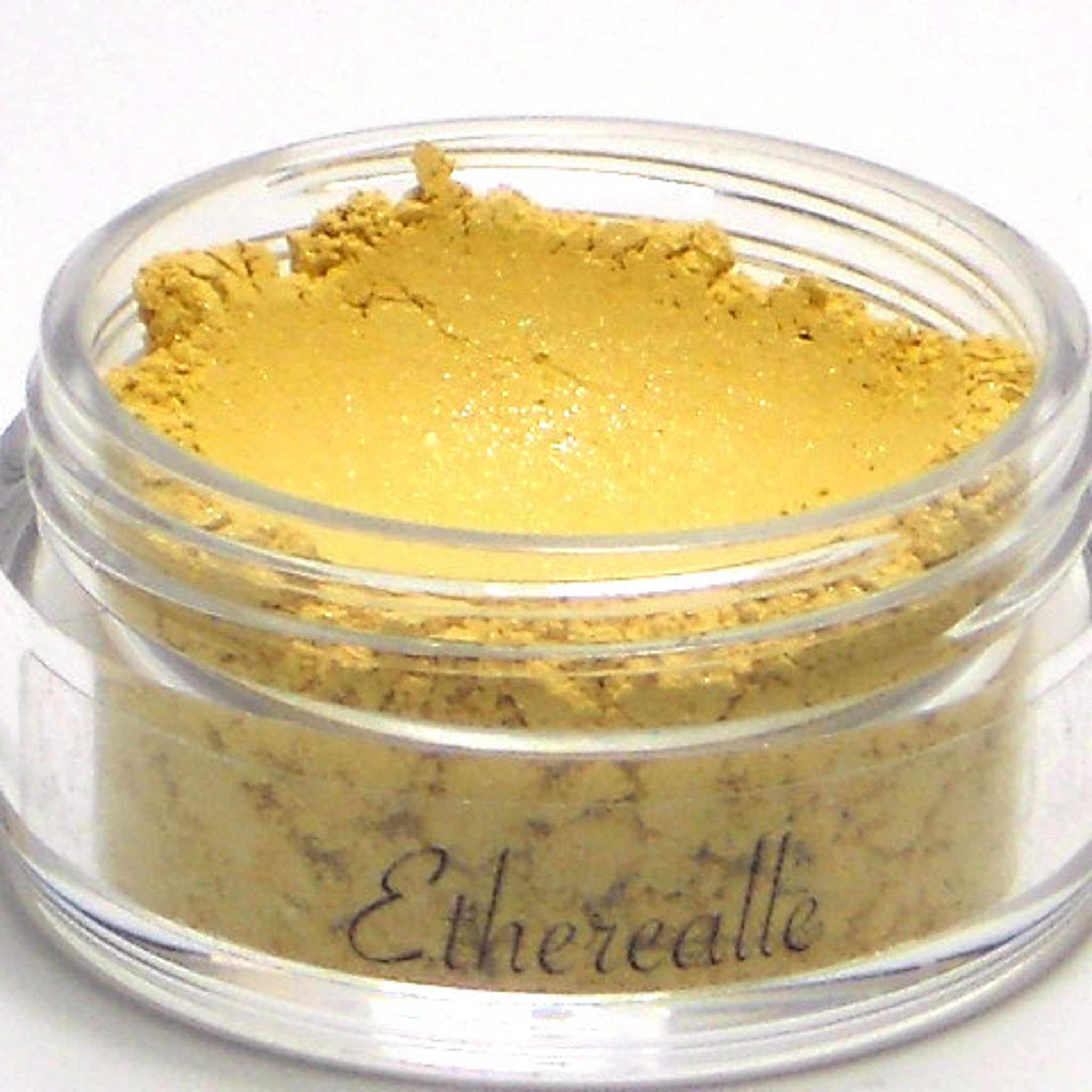 Powder makeup jar with yellow powder, clear plastic jar, and Etherealle text on the side