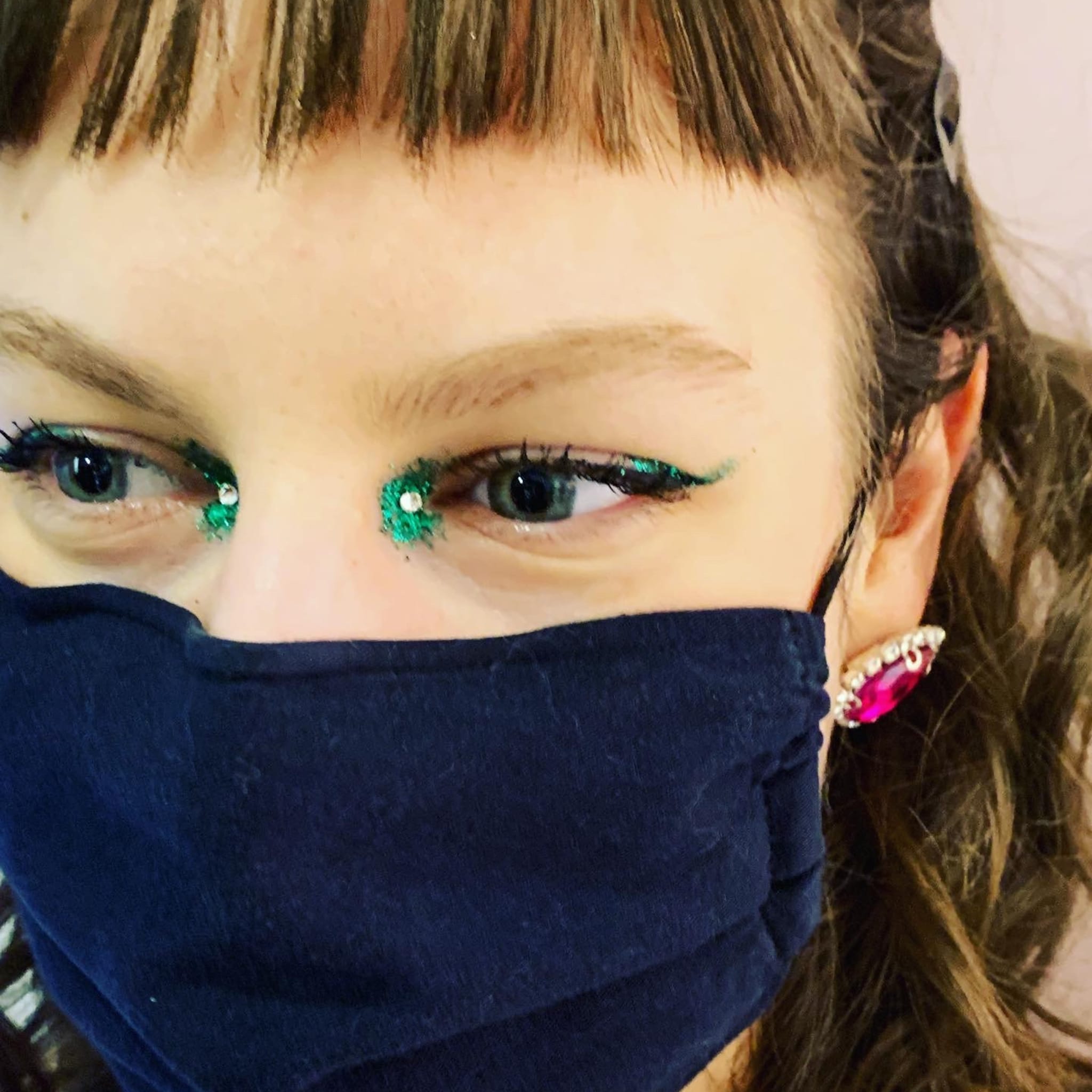 Face mask, blue fabric, woman wearing glitter eye makeup and pink earring, close-up shot