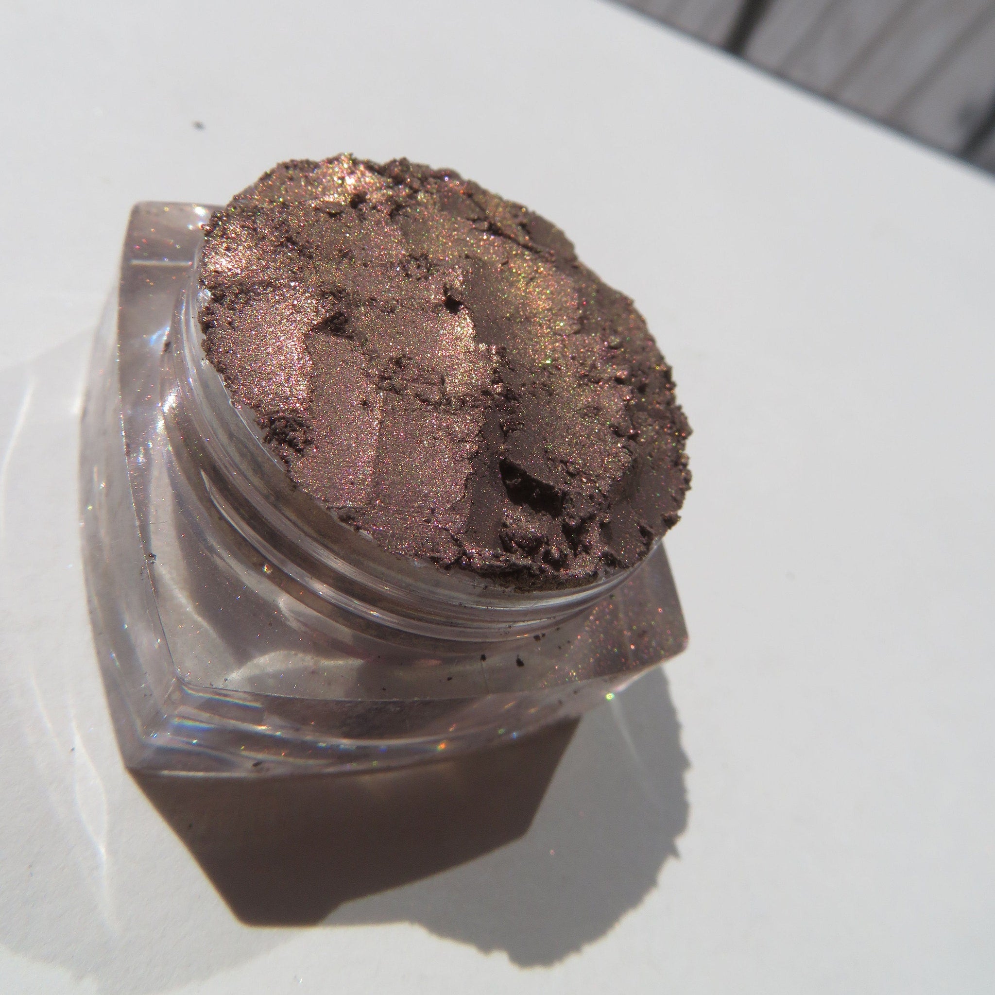 Close-up of loose mineral eyeshadow in shimmering dark brown with metallic rose undertones, vegan and talc-free