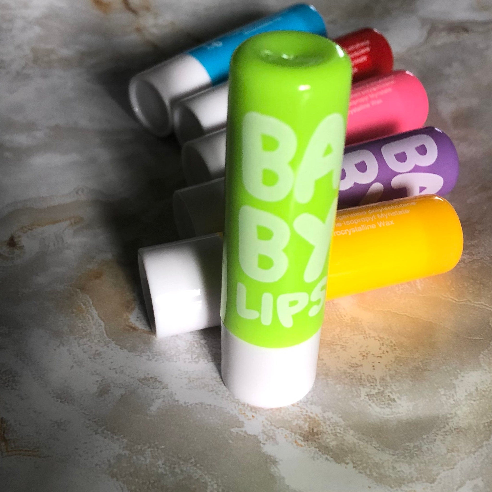 Lip balm tubes in various colors, including green, blue, pink, and yellow, with "BABY LIPS" text visible.