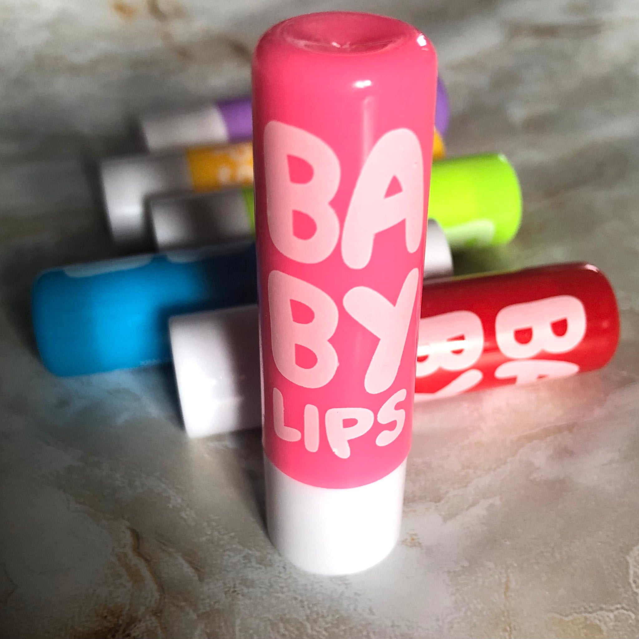 Lip balm, pink and white Baby Lips tube, with other colorful tubes in background