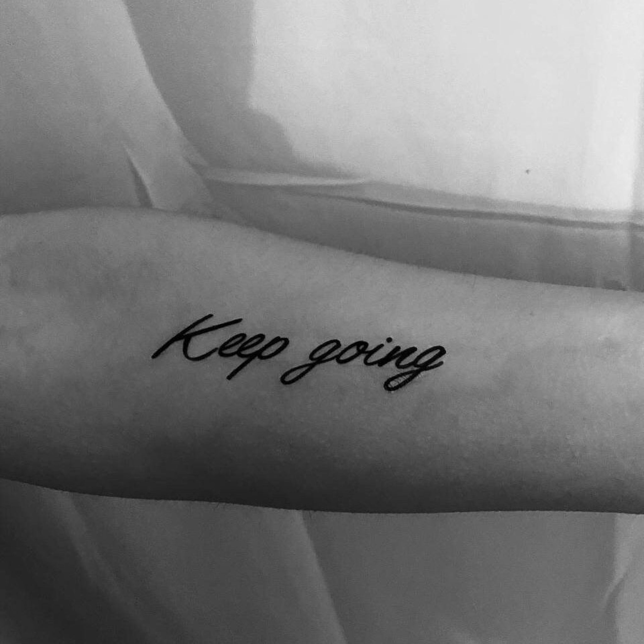 Temporary tattoo lettering, black script on arm, "Keep going" text