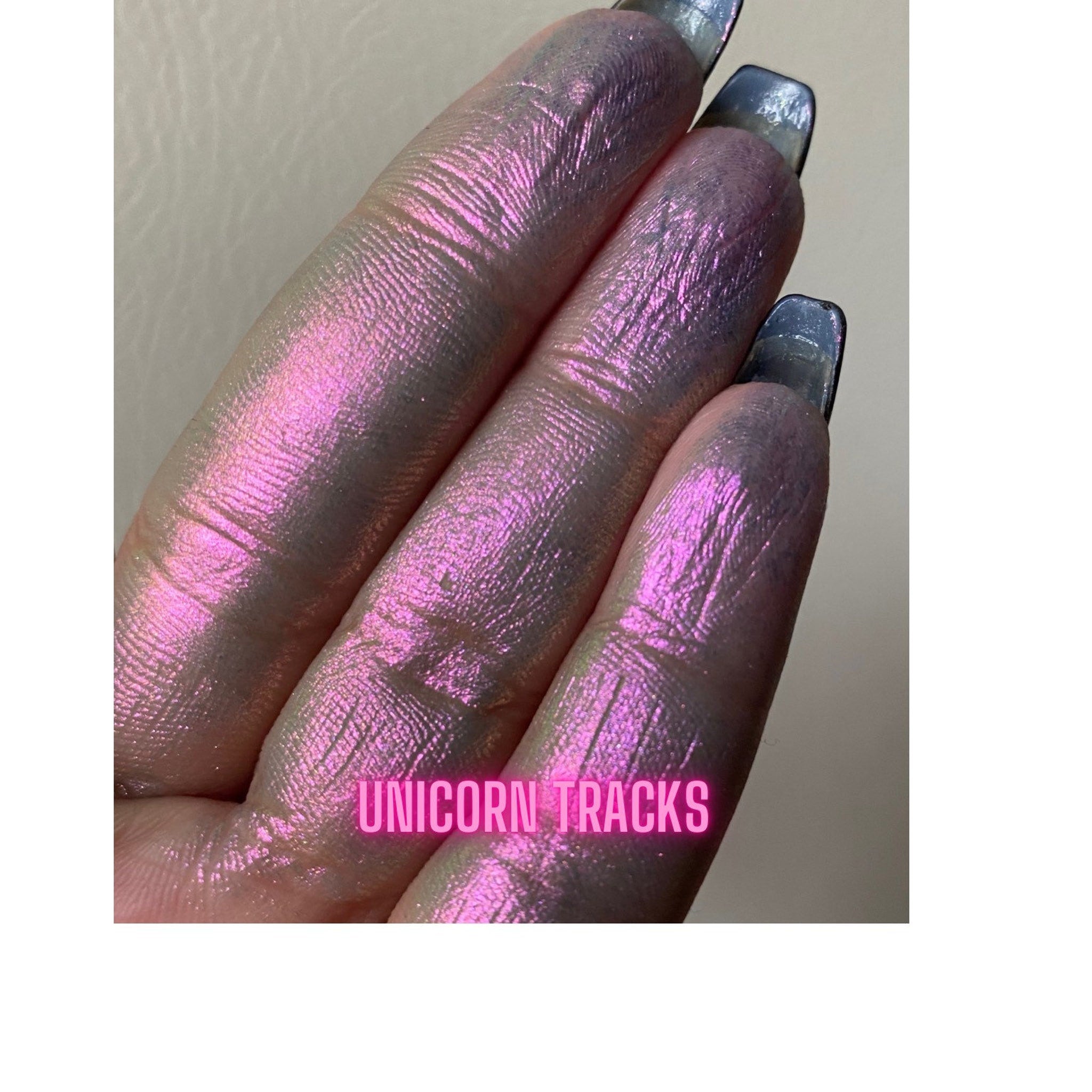 Hand applying multichrome unicorn eyeshadow with fingertip, showing iridescent shift from purple to green.