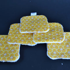 Reusable wipes with yellow geometric pattern and white trim, on black surface.