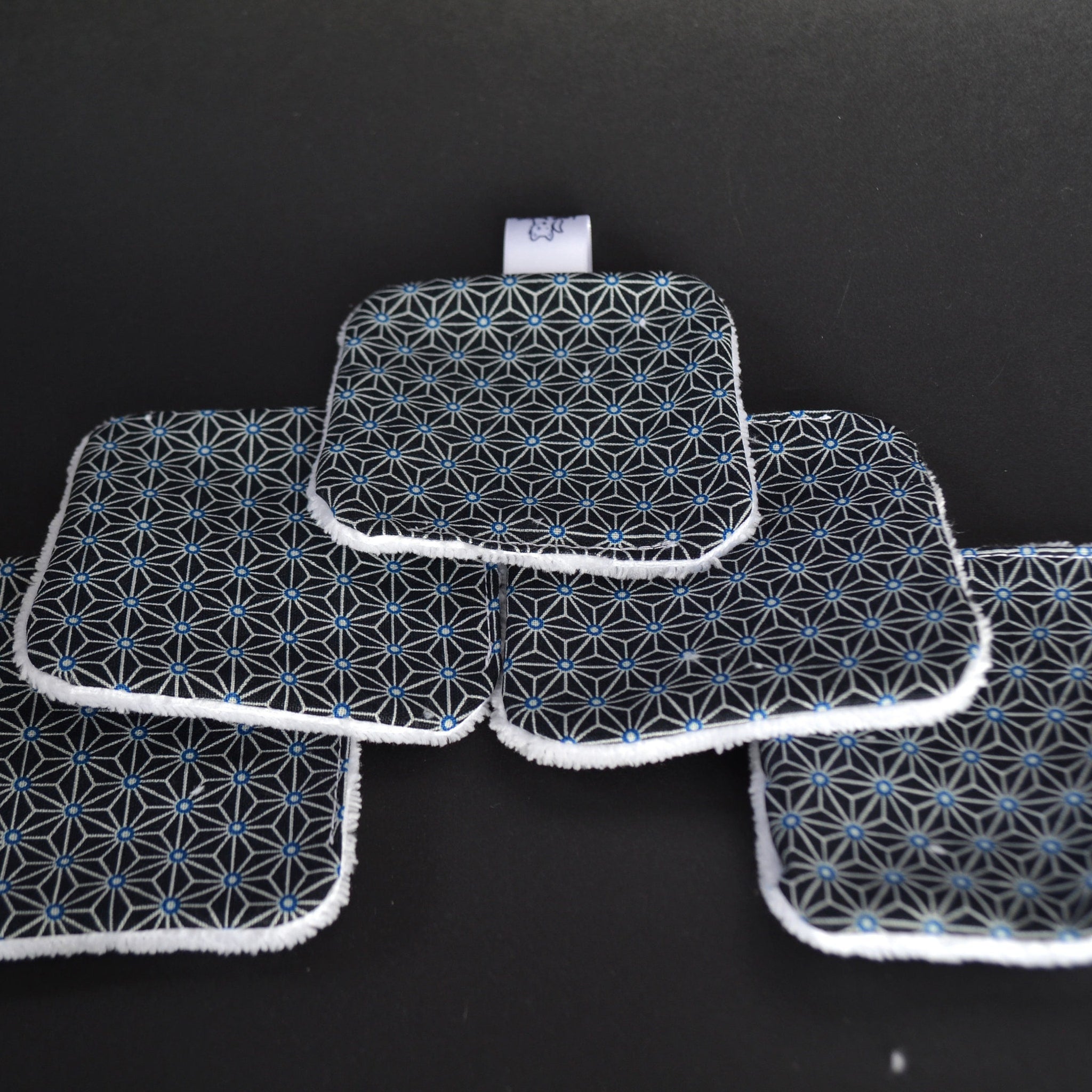 Reusable facial pads with black geometric pattern, blue accents, and white trim, on black background