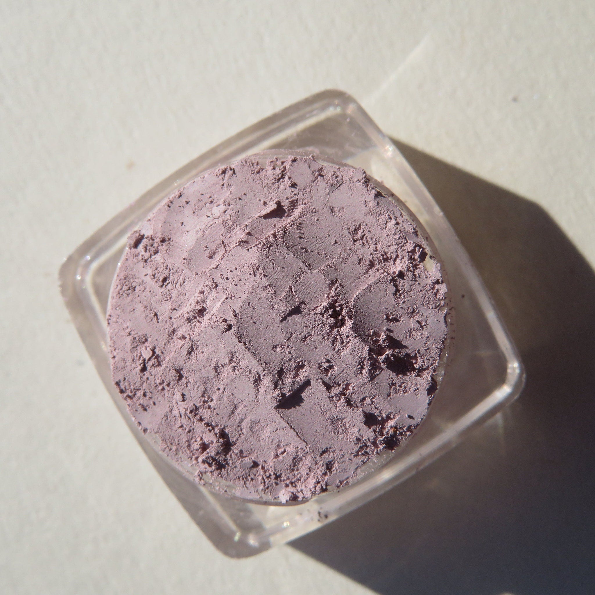 Open jar of muted pale purple matte mineral eyeshadow with loose powder visible inside