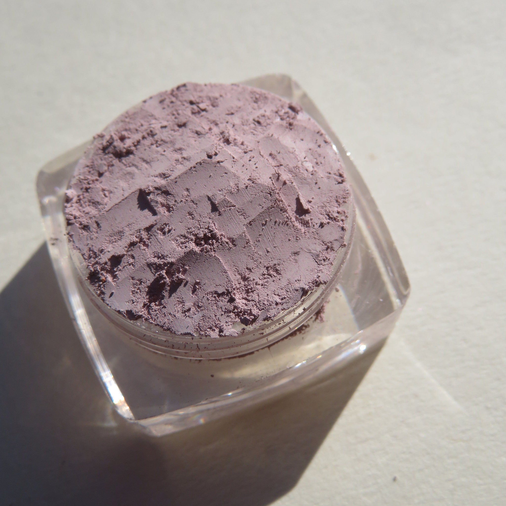 Swatch of muted pale purple matte mineral eyeshadow on fingertip showing soft powder texture